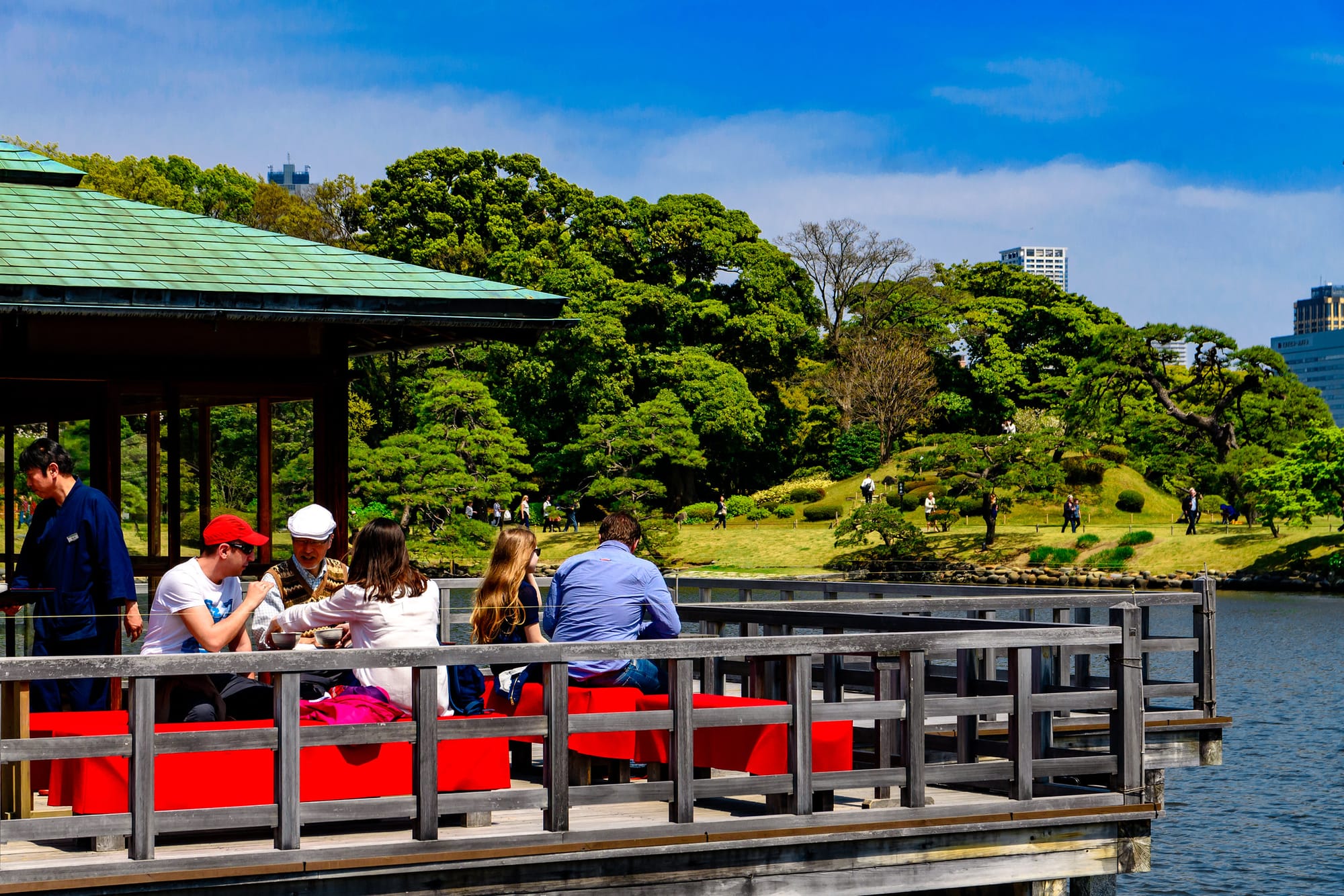 People sit on the deck of the Nakajima Teahouse, enjoying a green garden view.