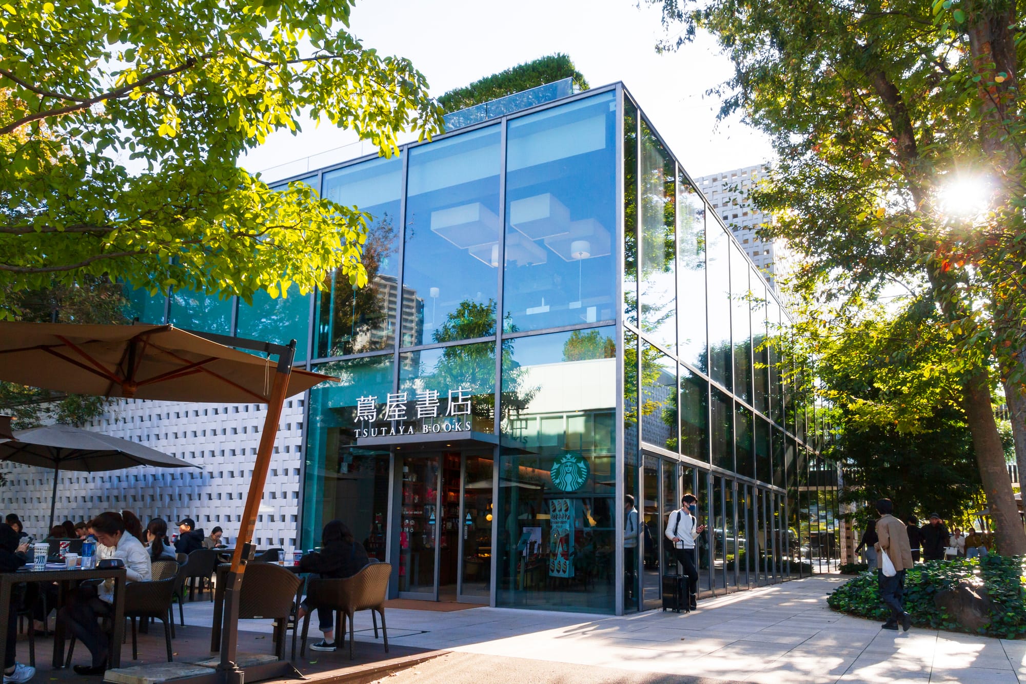Modern glass building of Tsutaya Books with outdoor seating beneath umbrellas.