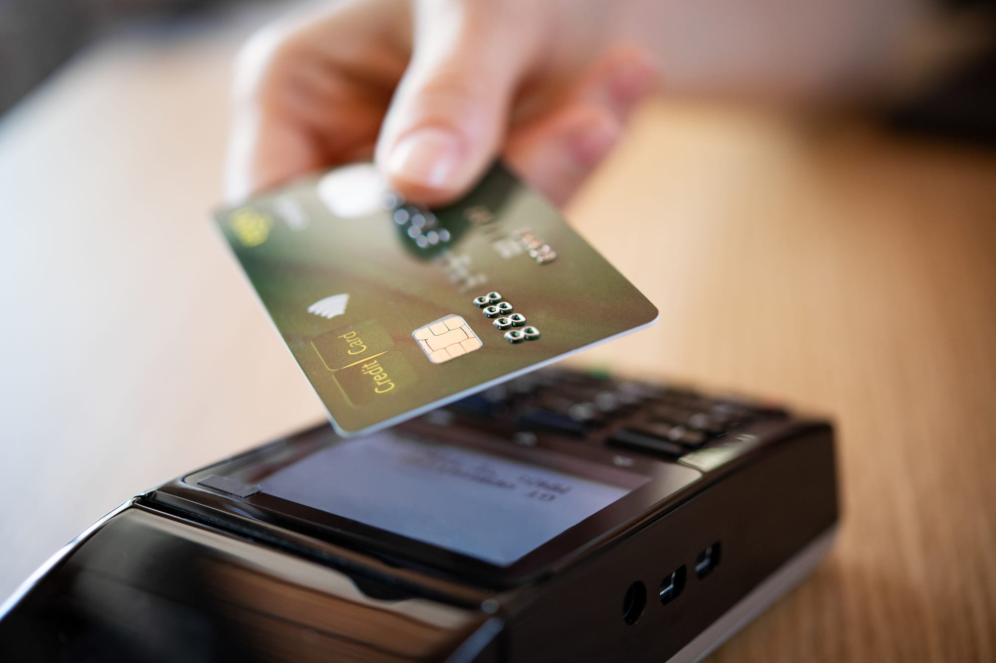 Hand holds green credit card near a black card reader.