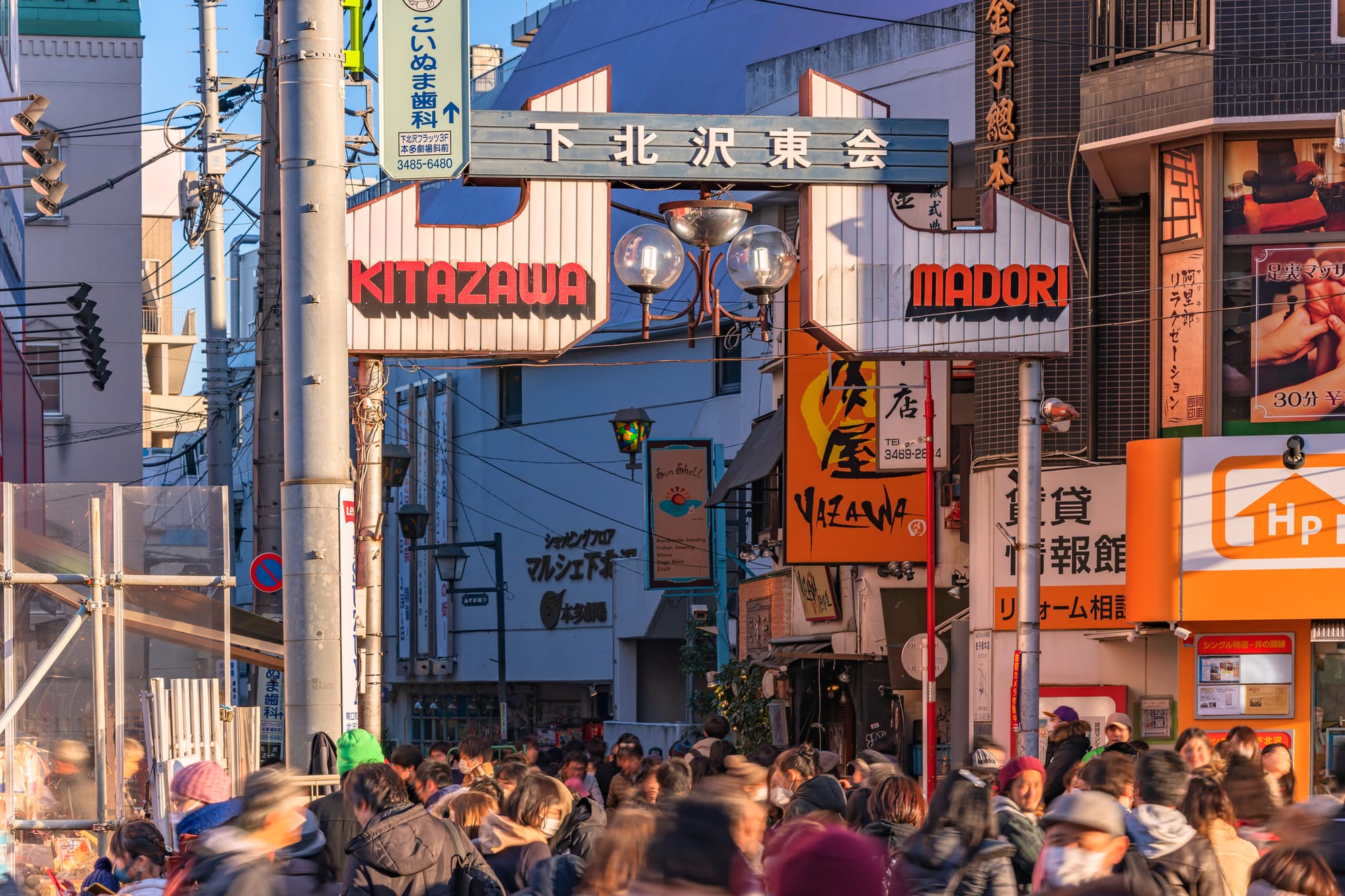 Bustling street scene with a crowd under signs of Shimokitazawa, reading "Kitazawa" and "Madori."