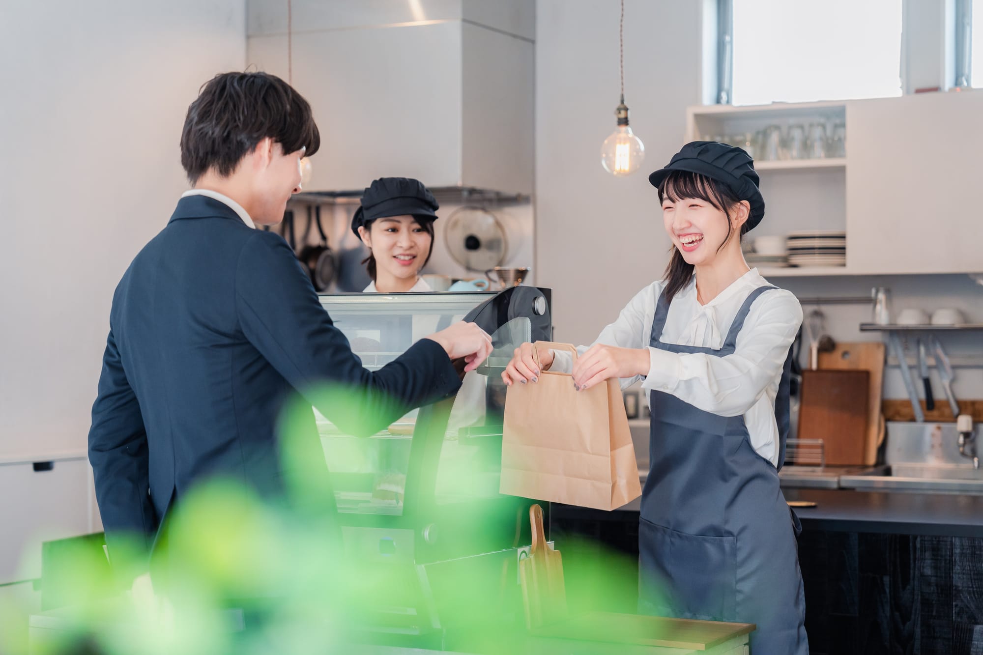 Barista in a cafe hands a takeout bag to a smiling customer.