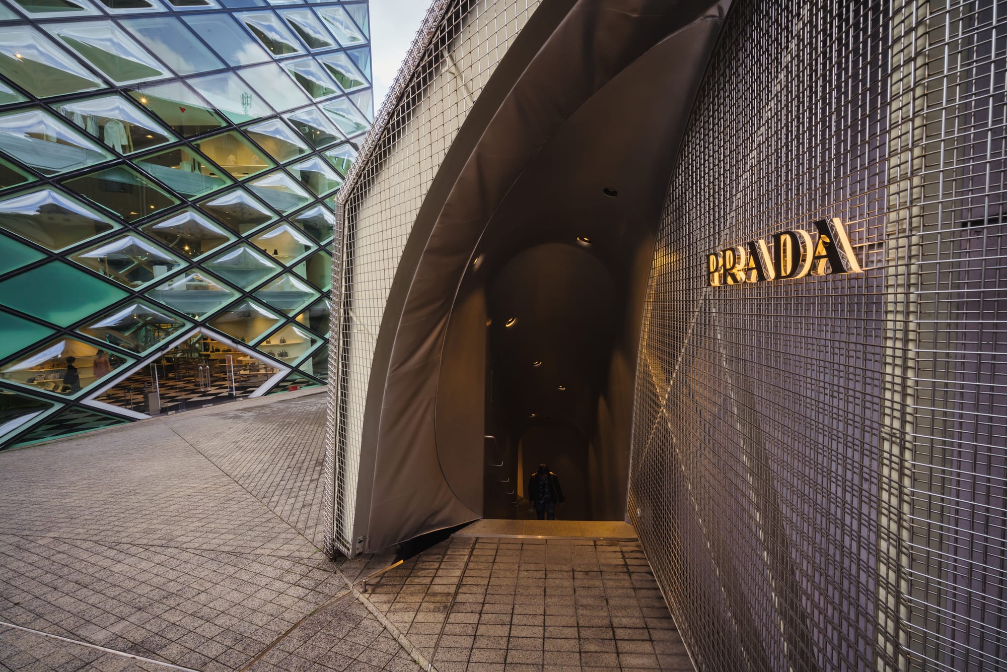 Modern building with diamond-patterned glass exterior. "PRADA" sign is illuminated.