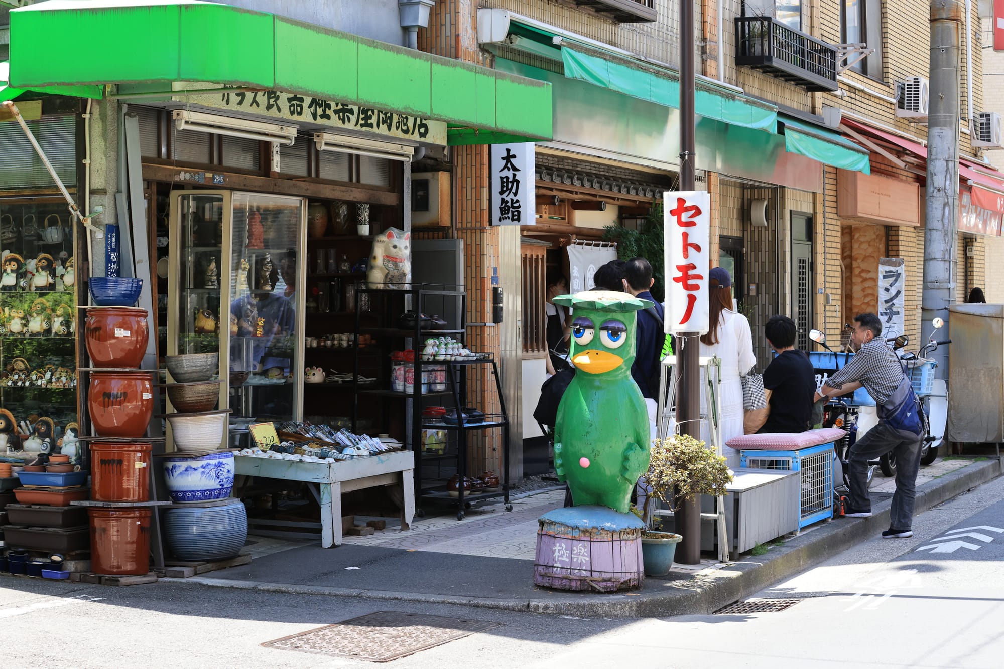 Kappabashi street shop with pottery and figurines. Green kappa statue in front.
