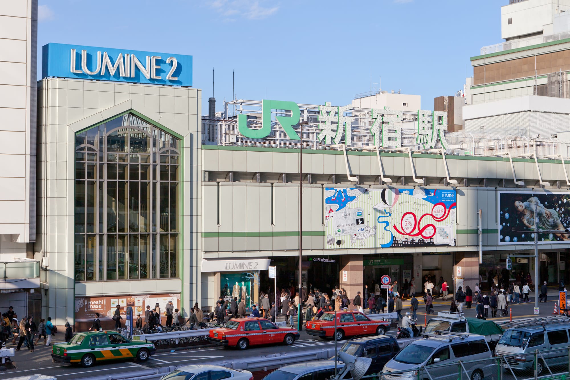 Shinjuku Station entrance with "LUMINE 2" sign, bustling crowd, taxis in red and green.