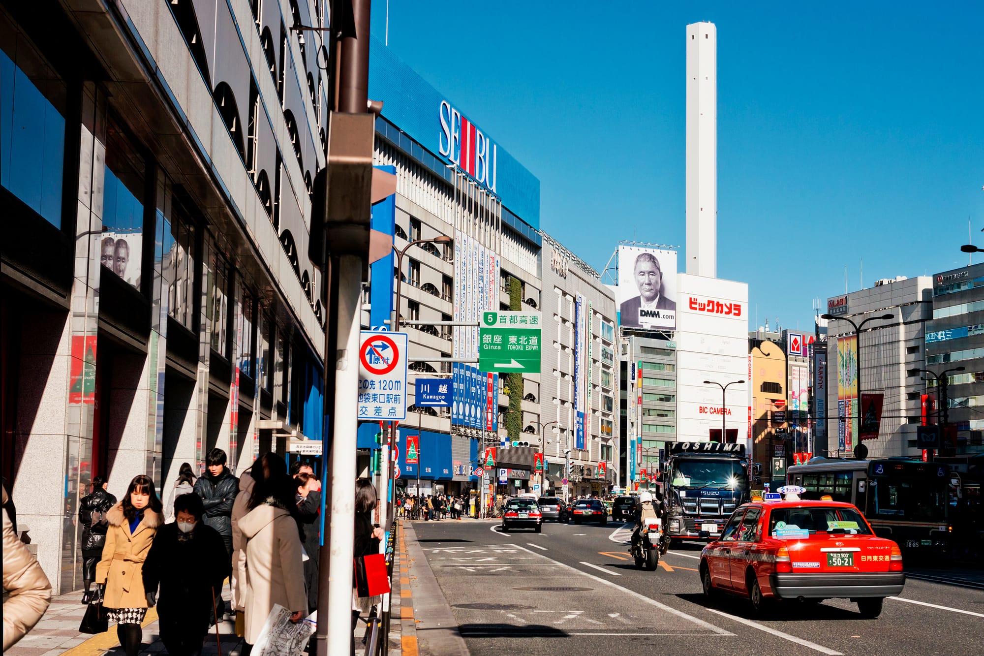 Busy city street in Ikebukuro with pedestrians, bikes, and cars. 