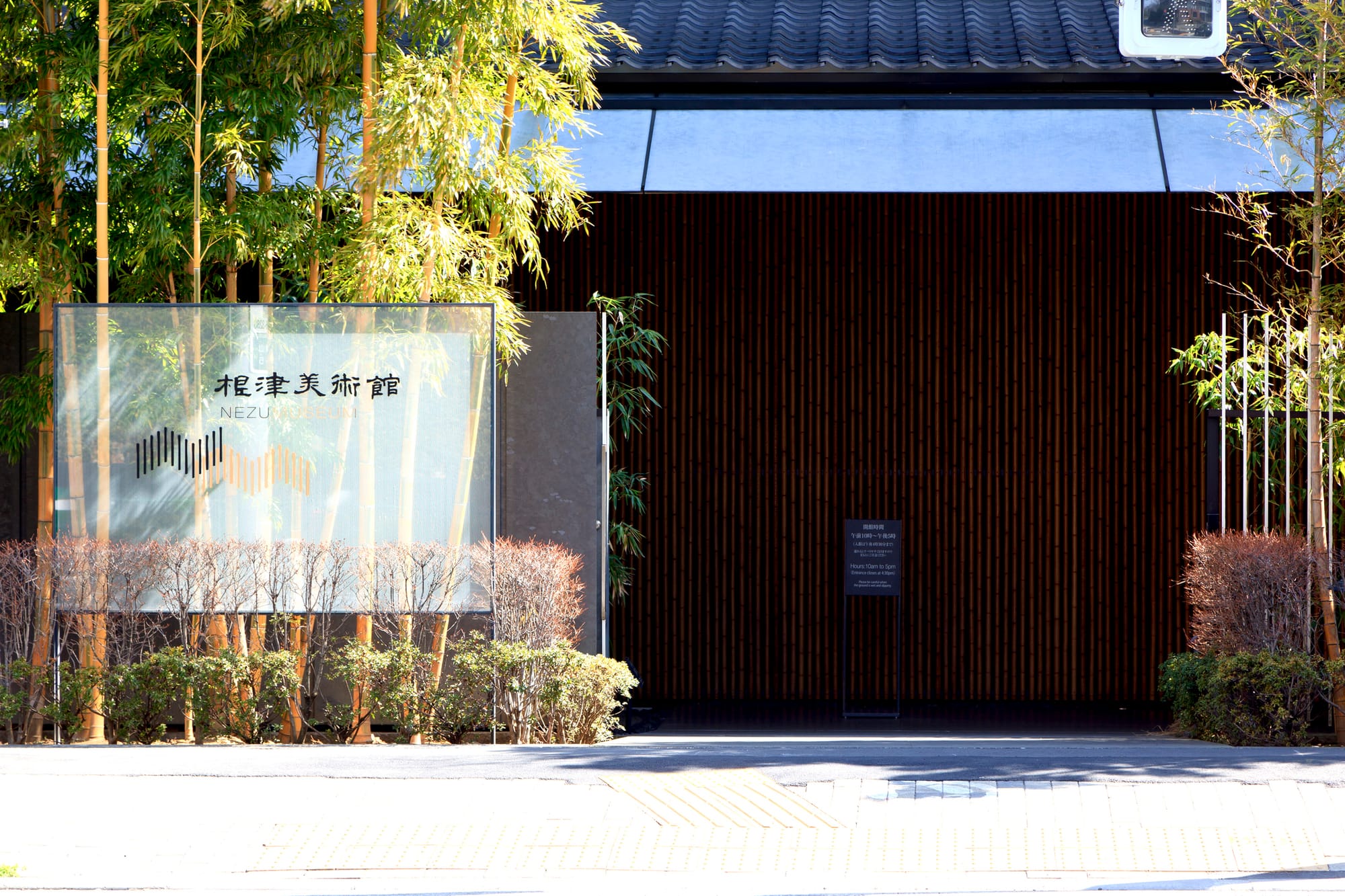 Entrance of Nezu Museum, bamboo and shrubs in foreground, and dark wooden facade.