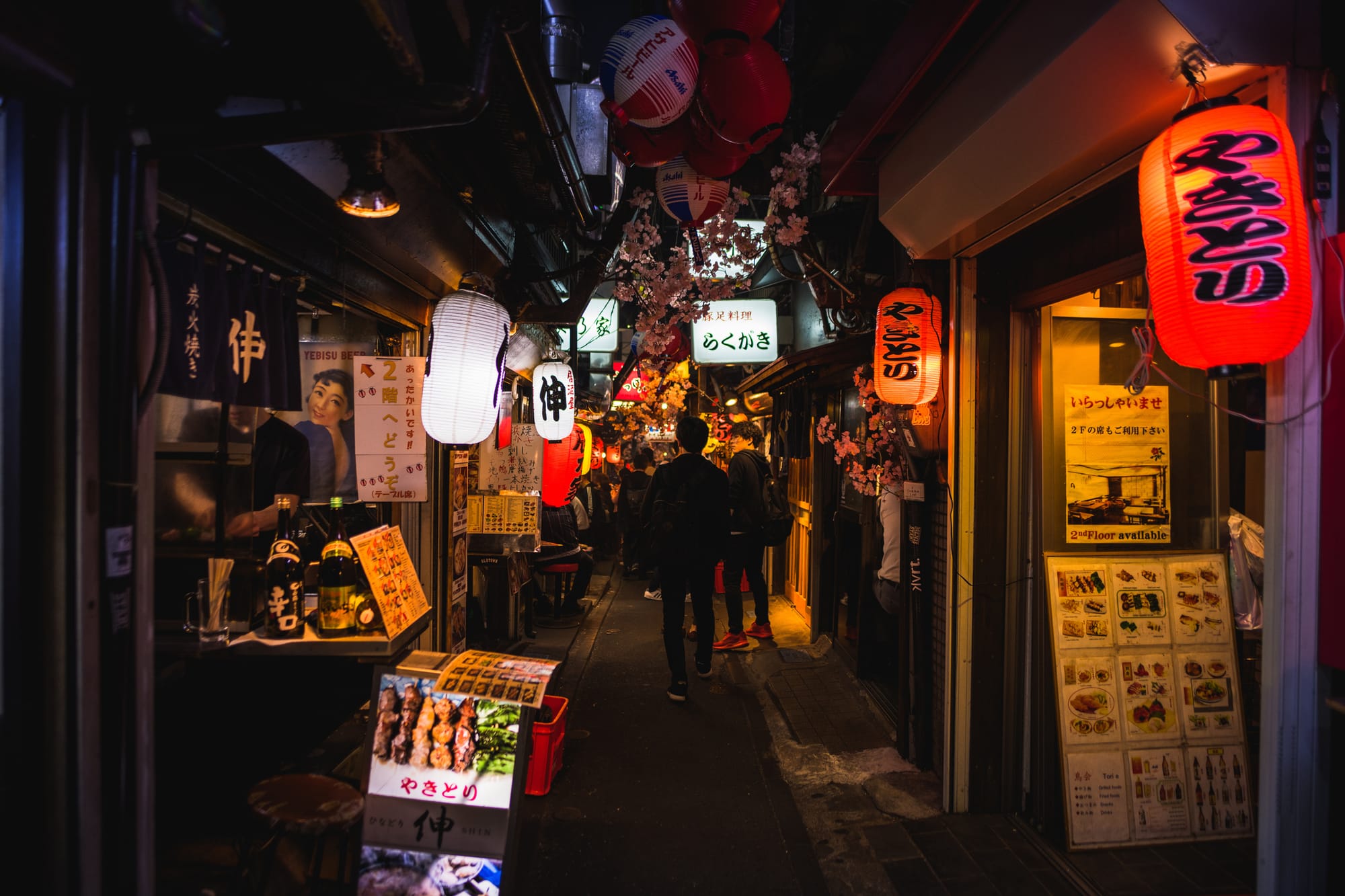 Omoide Yokocho alley with people walking, lined with vibrant red and white lanterns.