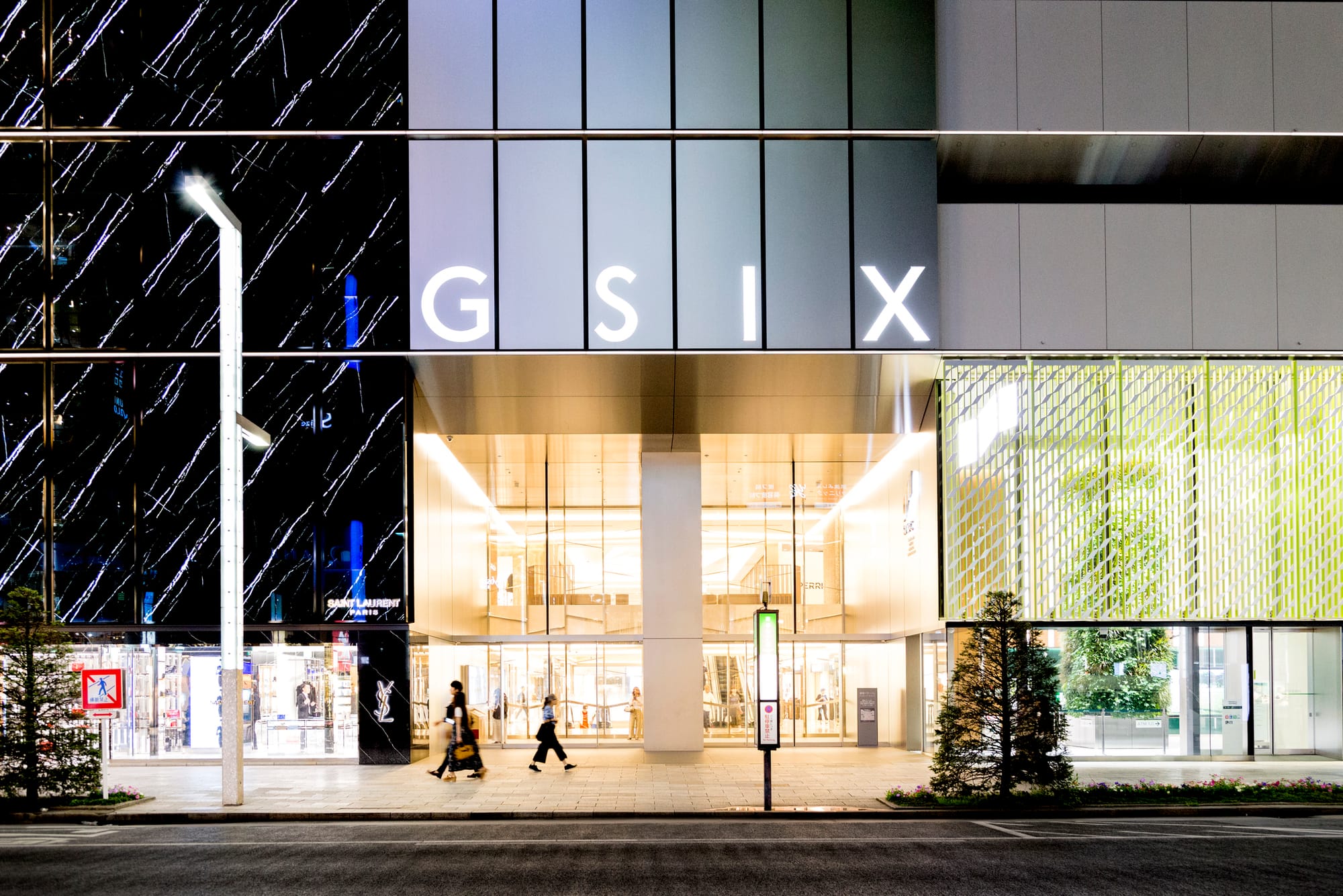 Modern building exterior at night with "GSIX" sign, glass facade, and trees.