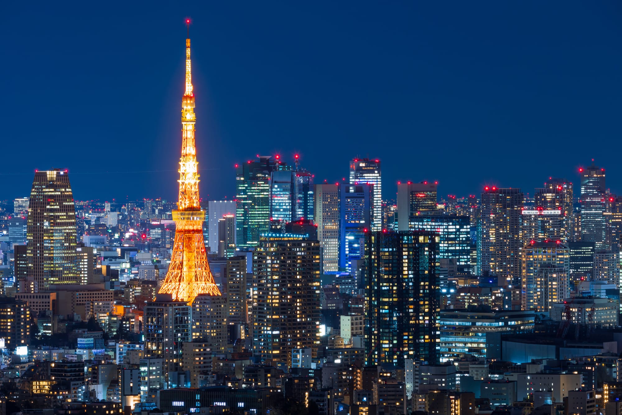 City view of Tokyo with an orange Tokyo Tower glowing in between tall buildings.