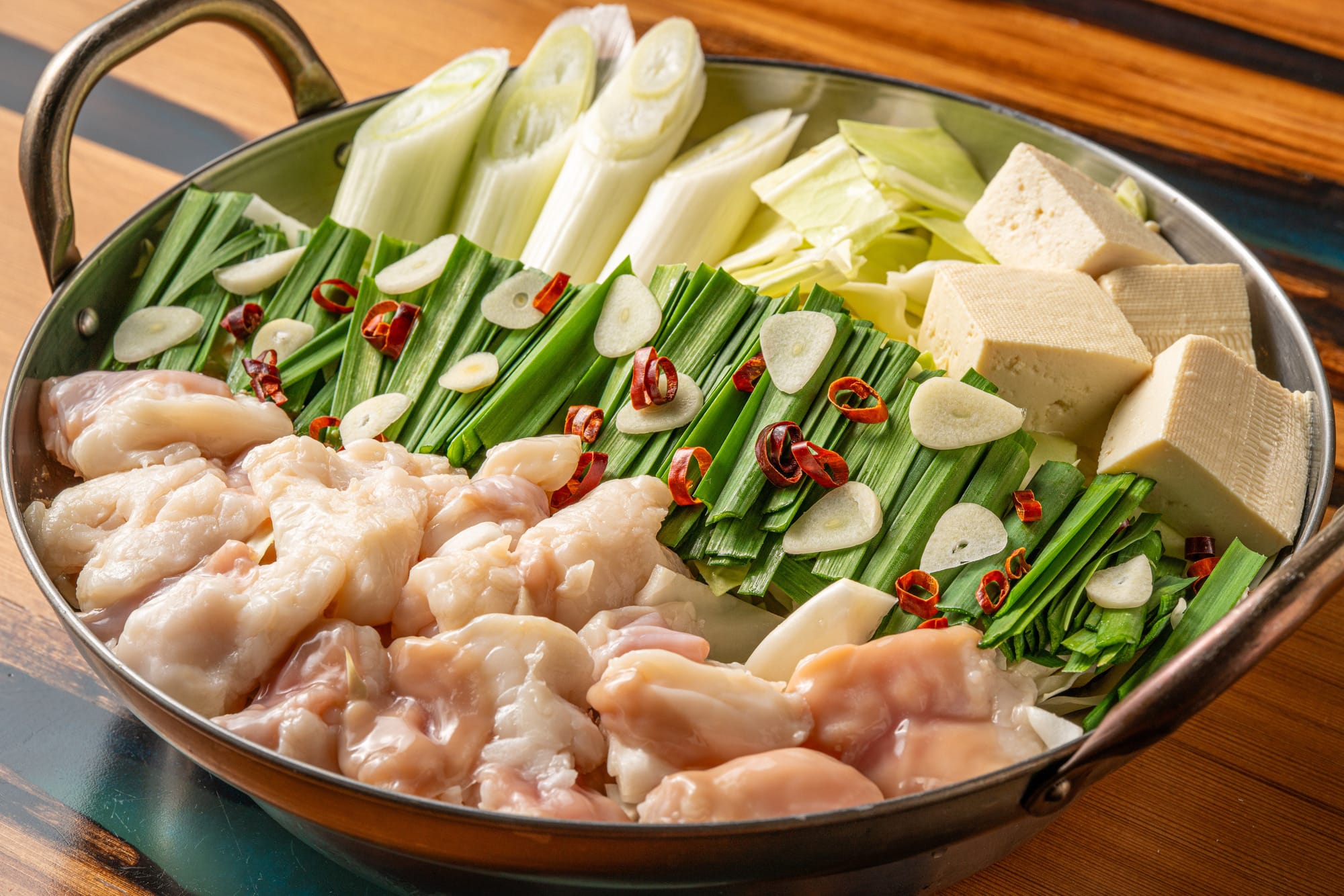 Matsunabe hot pot with chicken, leeks, tofu, garlic, and chili on a wooden table.