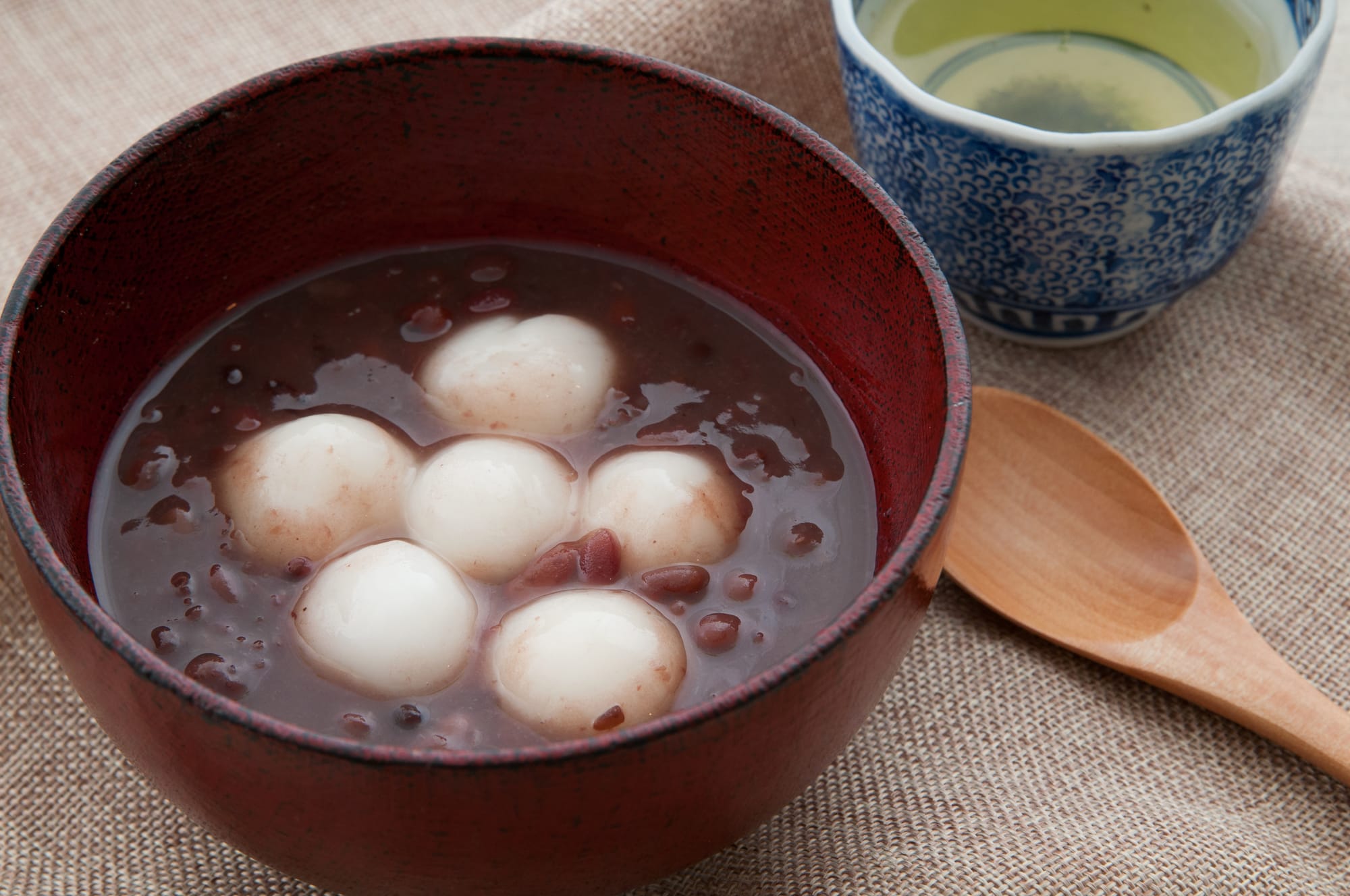 A bowl of Zenkai with mochi in red bean soup next to a blue cup of green tea