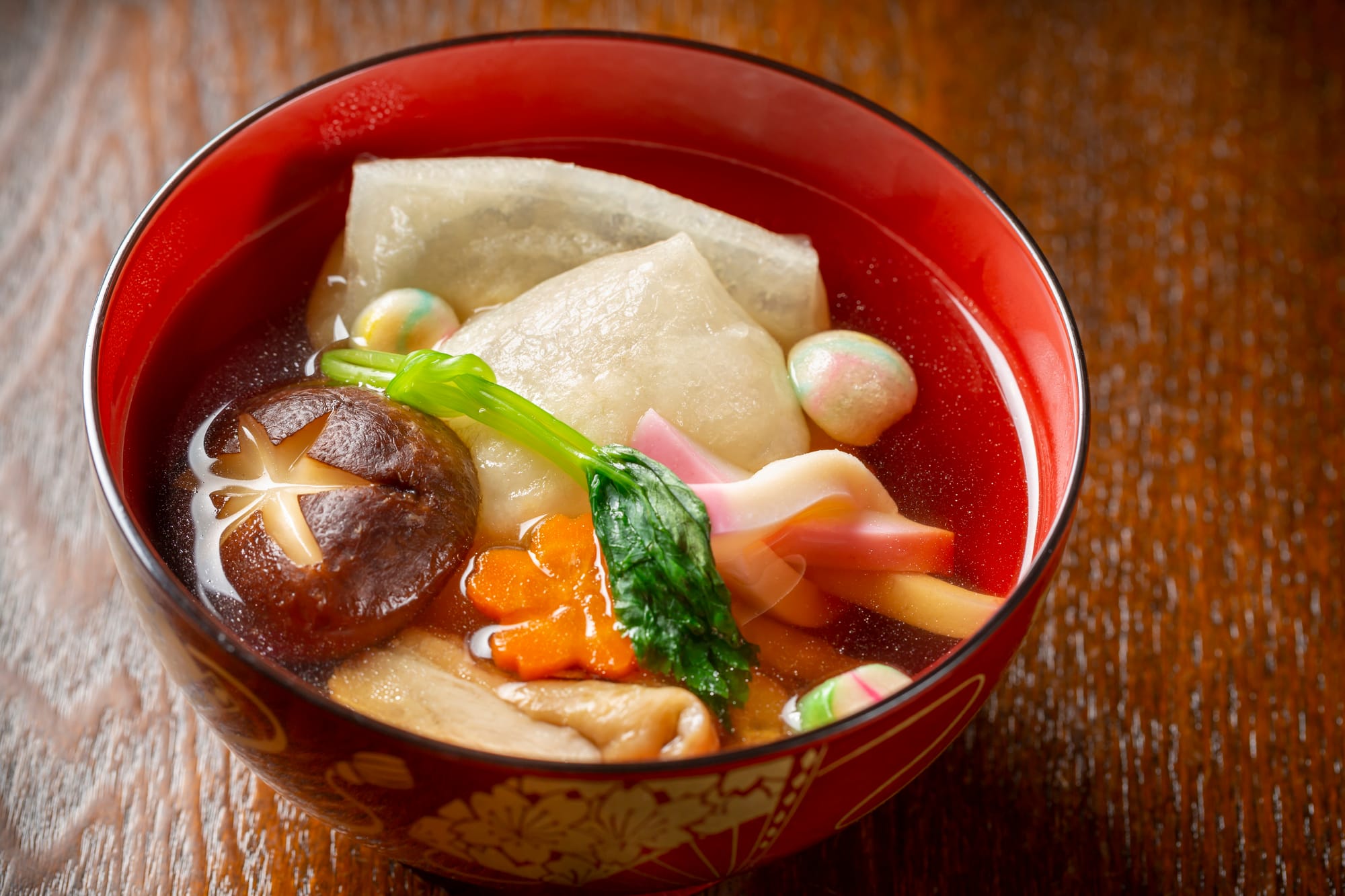 A bowl of ozoni with mochi, shiitake mushroom, greens, and carrot.