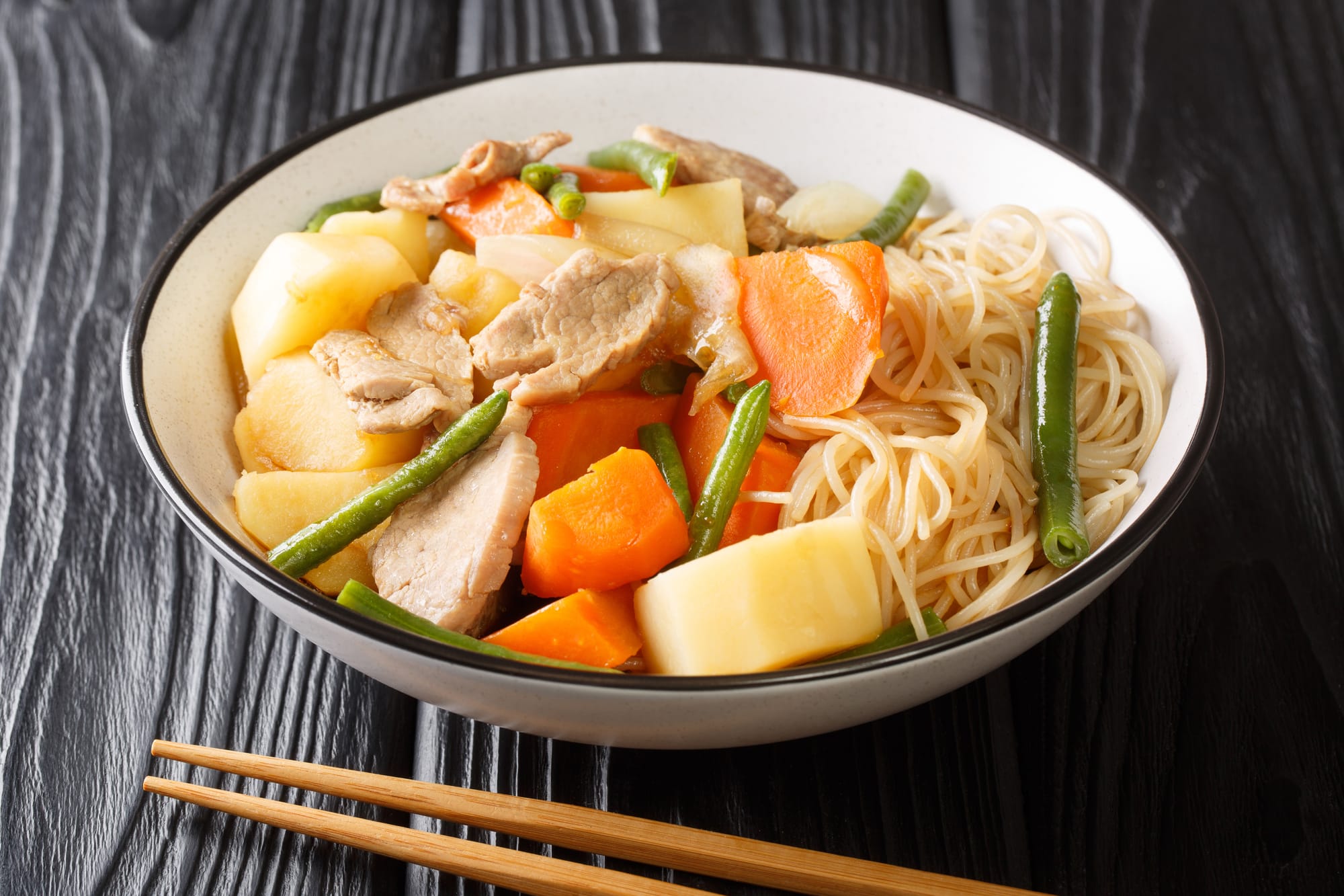 Bowl of nikujaga with pork, carrots, potatoes, and green beans, served with noodles. 