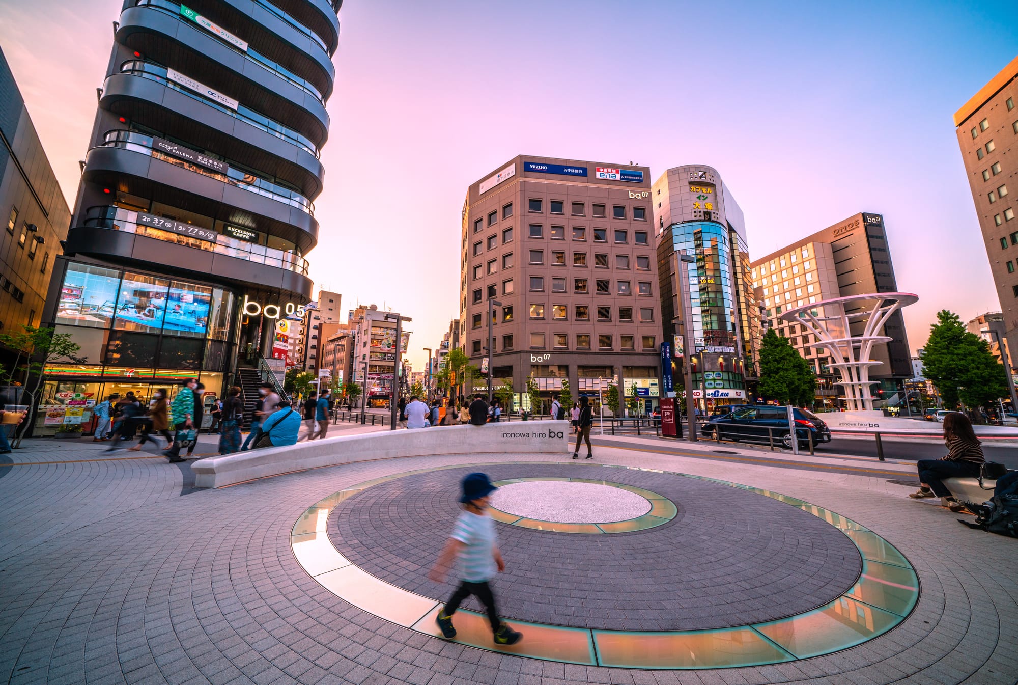 City scene at dusk with people walking in a plaza at Otsuka station. 
