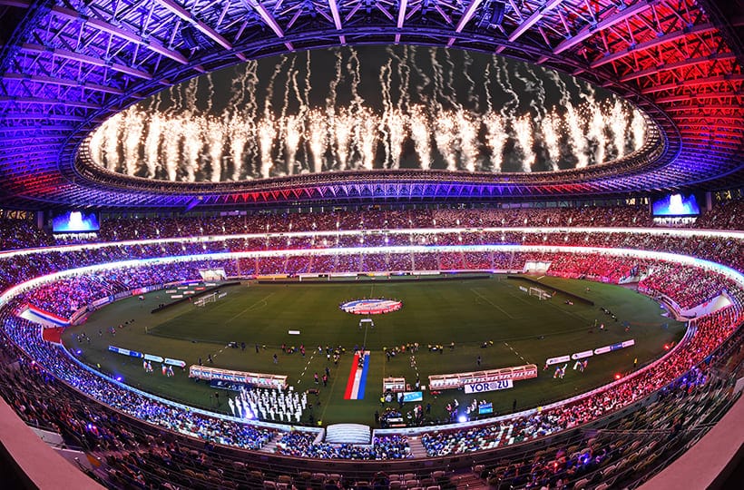 Tokyo National Stadium with colorful lights and fireworks, full crowd.