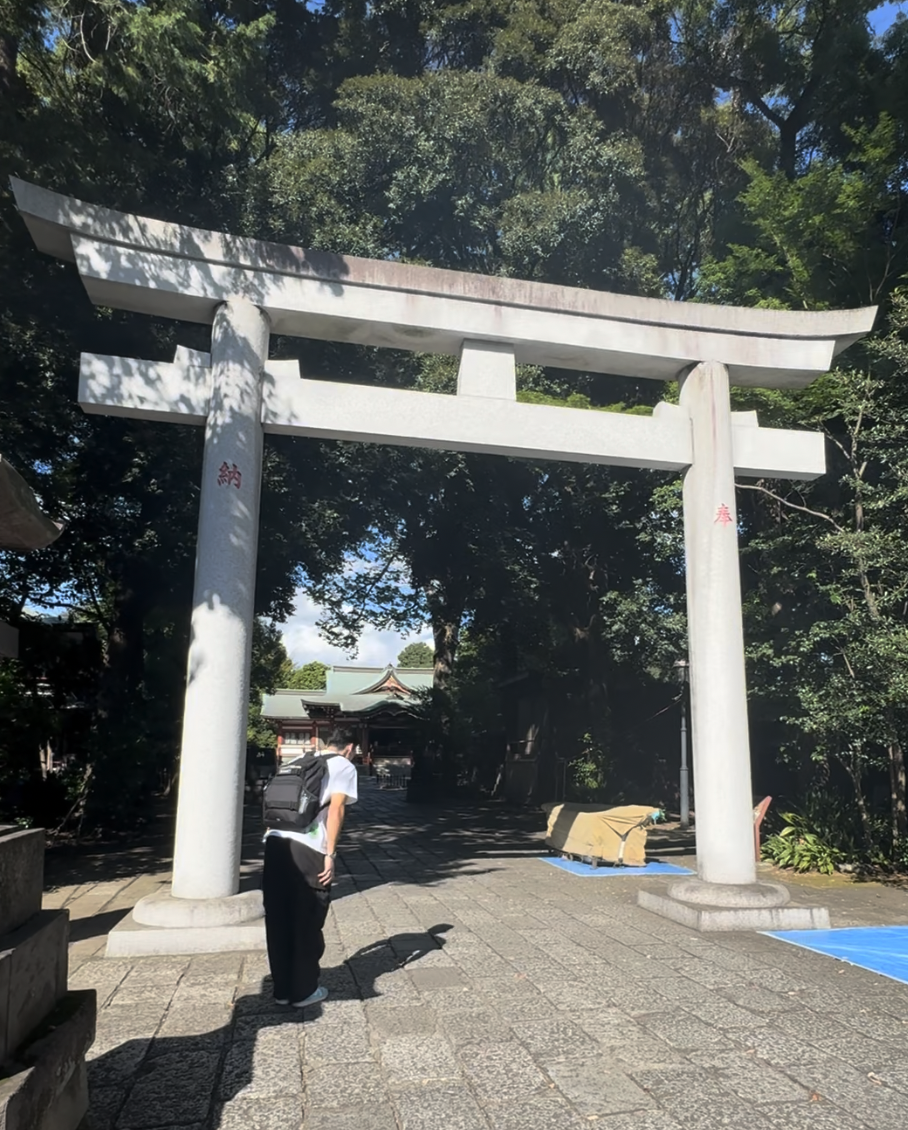 A young Japanese man bowing in front of the entrance of a Japanese shrine in a park.