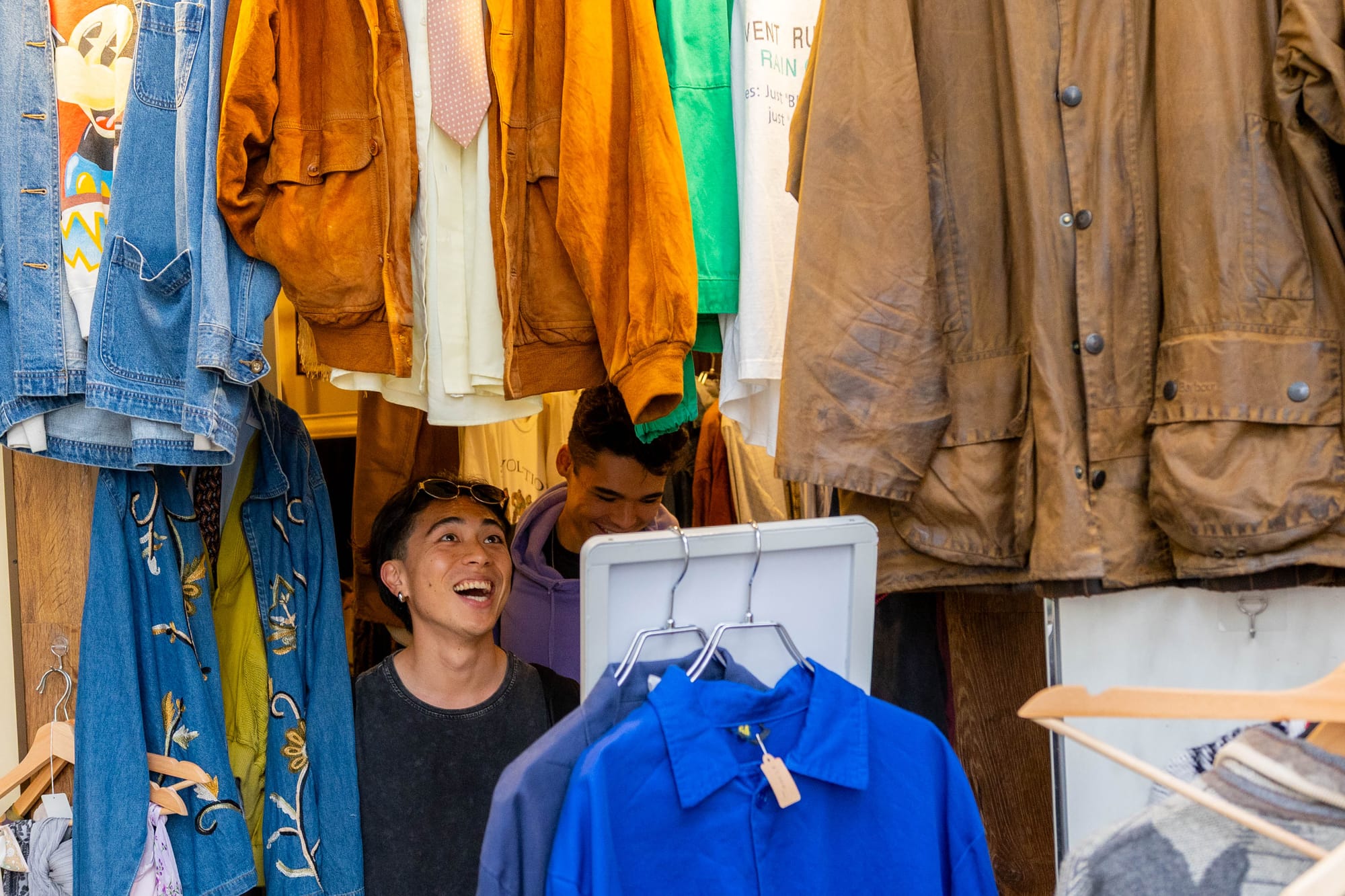 Two men in a vintage clothing shop in Koenji surrounded by colorful jackets, including denim and leather. 