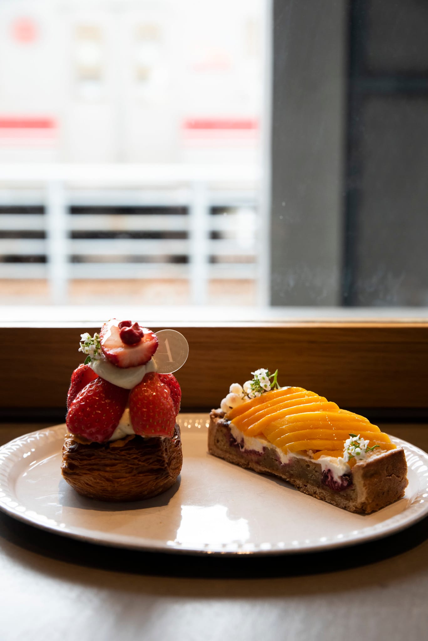 Pastries on a white plate; a strawberry-topped croissant and a mango slice tart with cream.