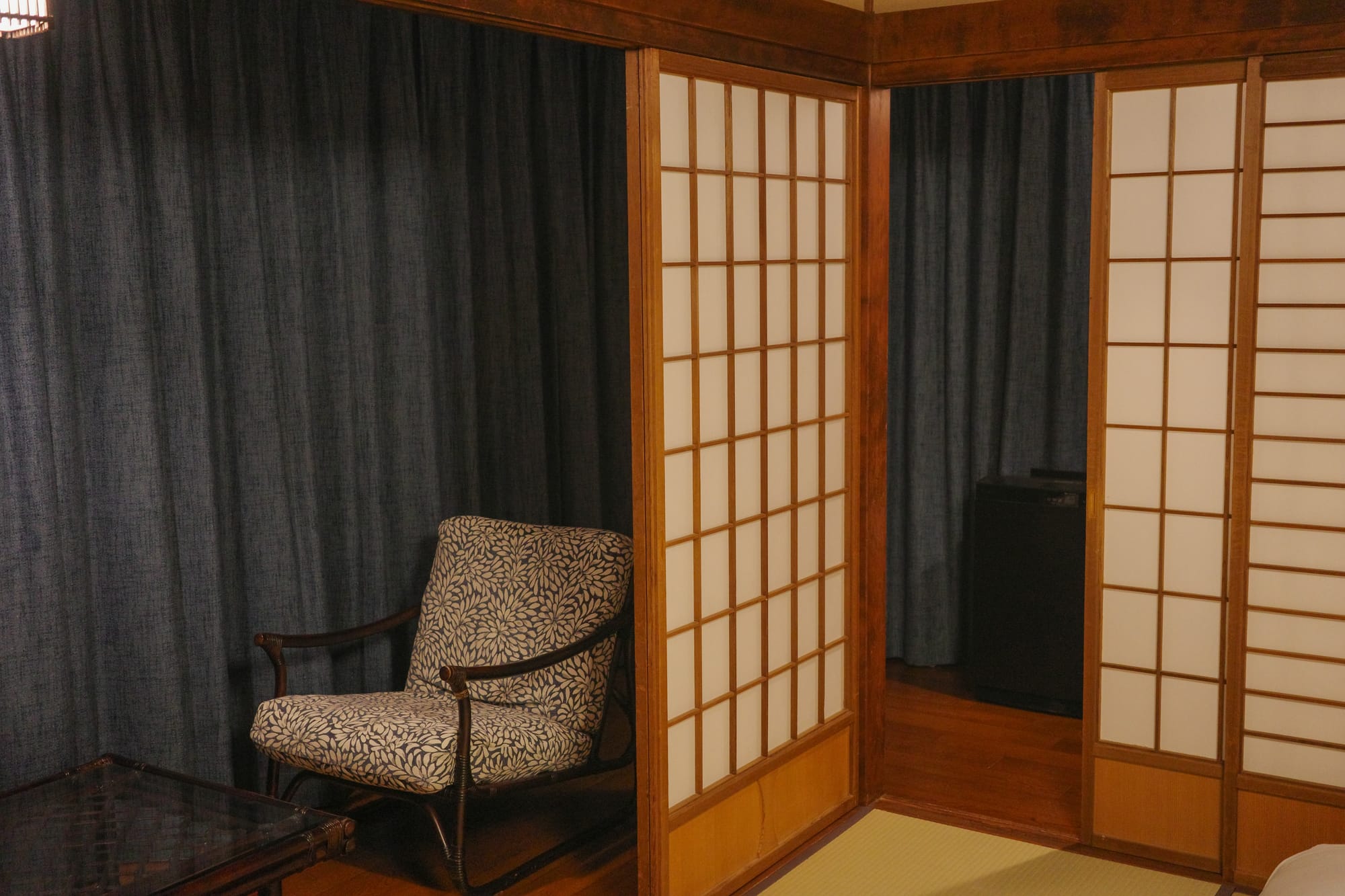 A cozy room with shoji screens, a patterned armchair, and dark curtains
