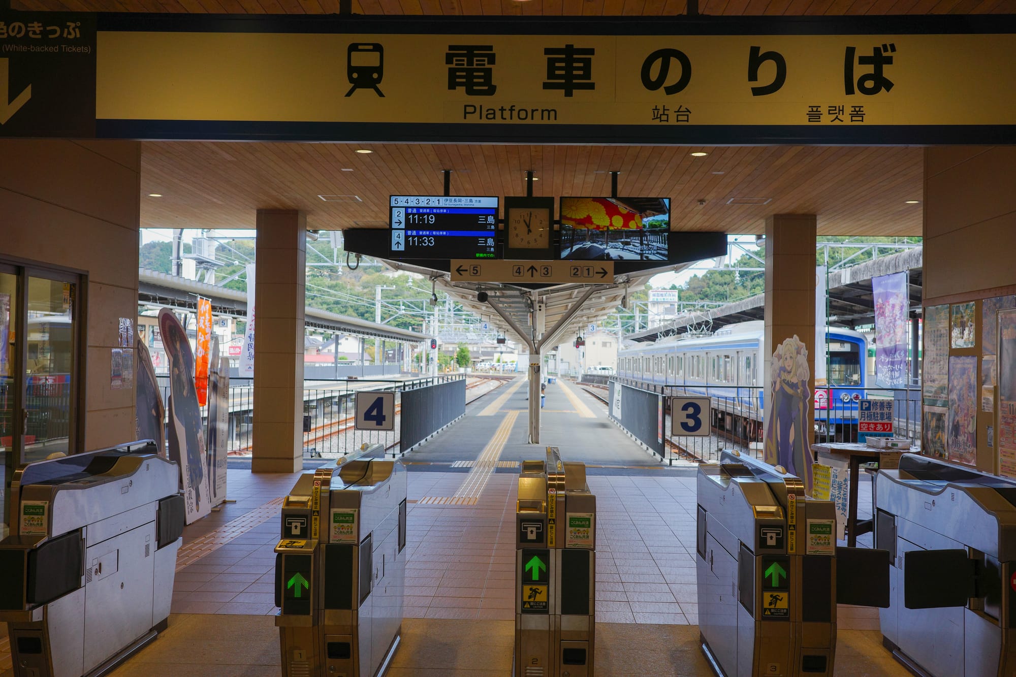 Train station platform with ticket gates, digital schedule showing times, and train on the track.