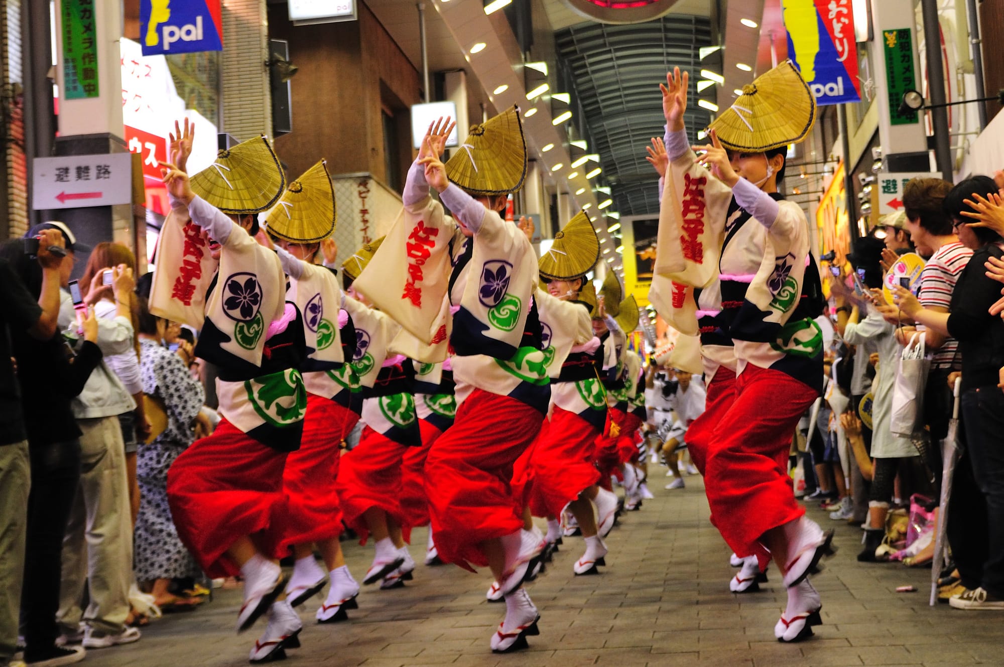 Dancers in traditional kimono-outfits and straw hats perform the Awa Odori dance in the middle of a shopping street, as spectators watch