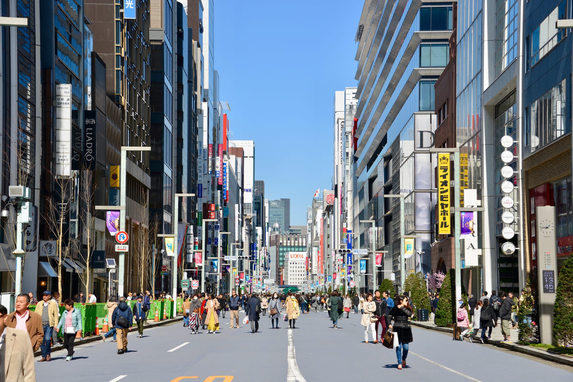 Busy Ginza street with people walking along a road flanked by tall buildings.