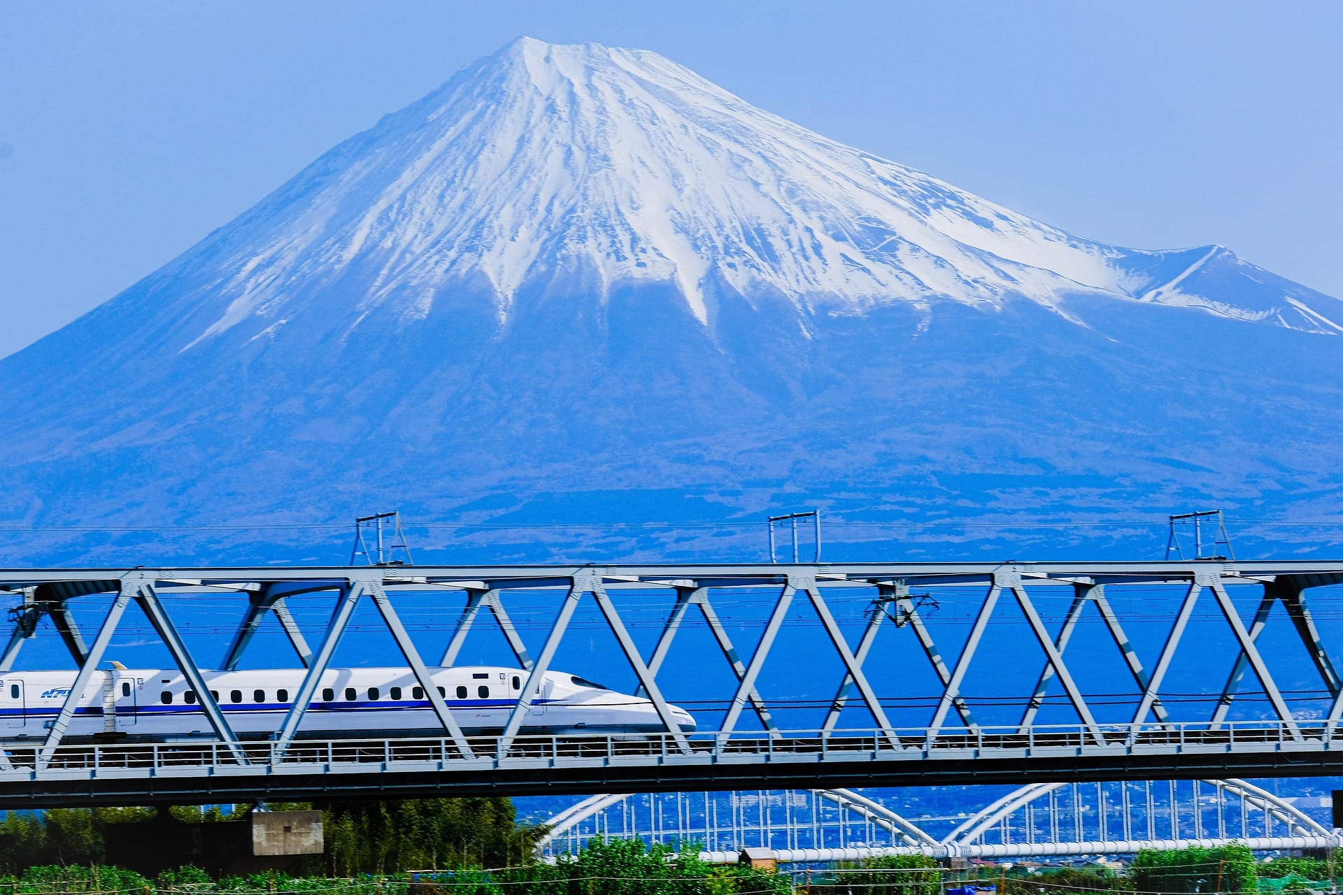 A Shinkansen bullet train passing through a bridge, with Mt. Fuji in the background