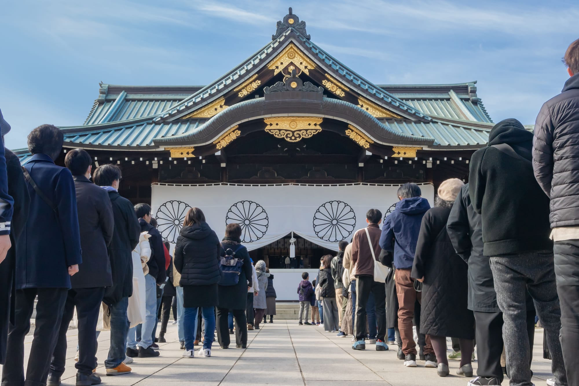 People line up outside a traditional Japanese building with a blue roof. 