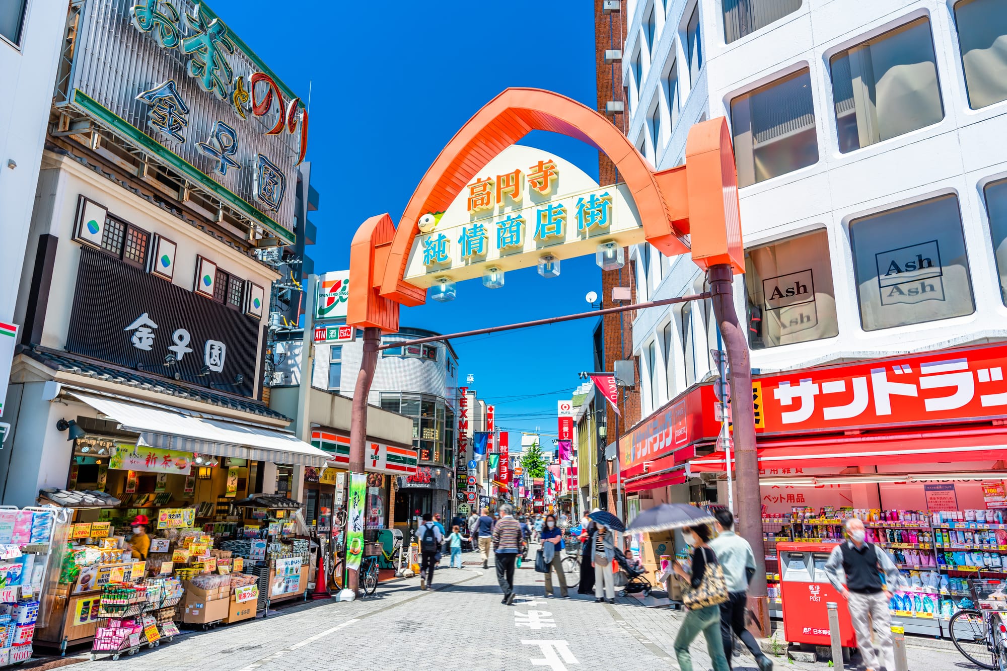 Koenji shopping street with people walking under an orange archway. Vibrant signage.