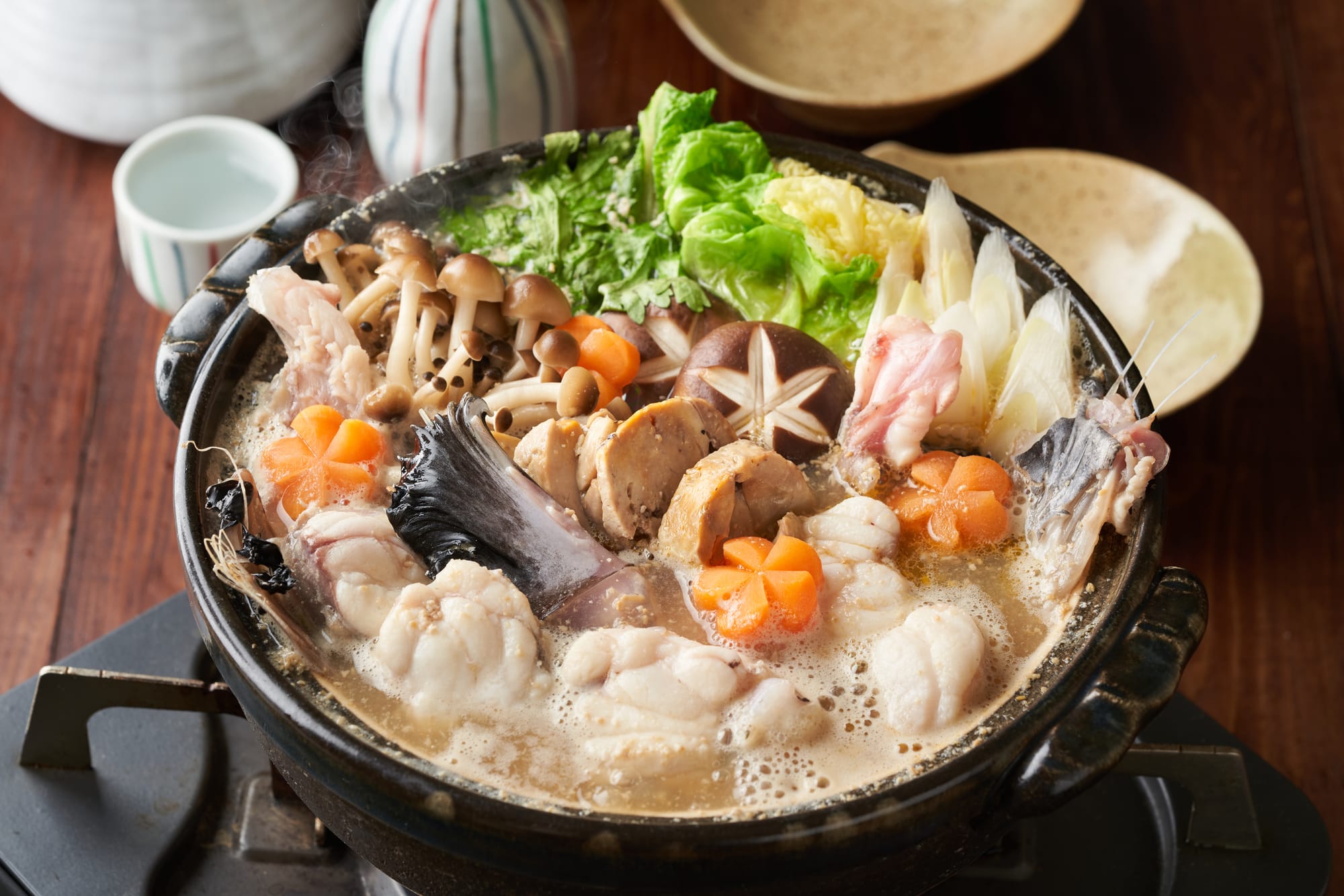 A steaming hot pot with fish, mushrooms, greens, and vegetables in a broth. 