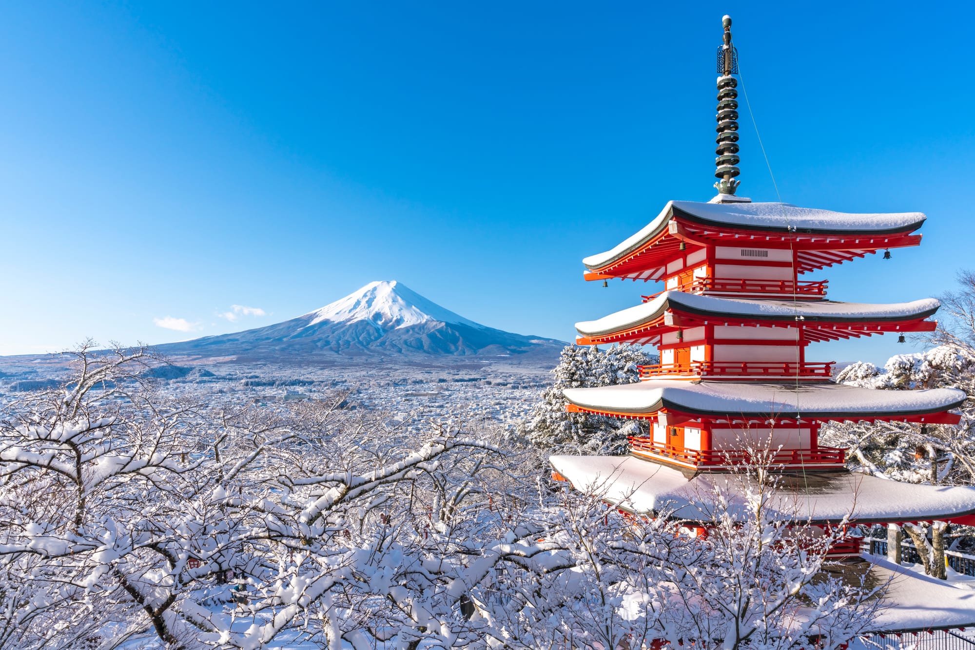 Red pagoda covered in snow with Mount Fuji in the background.
