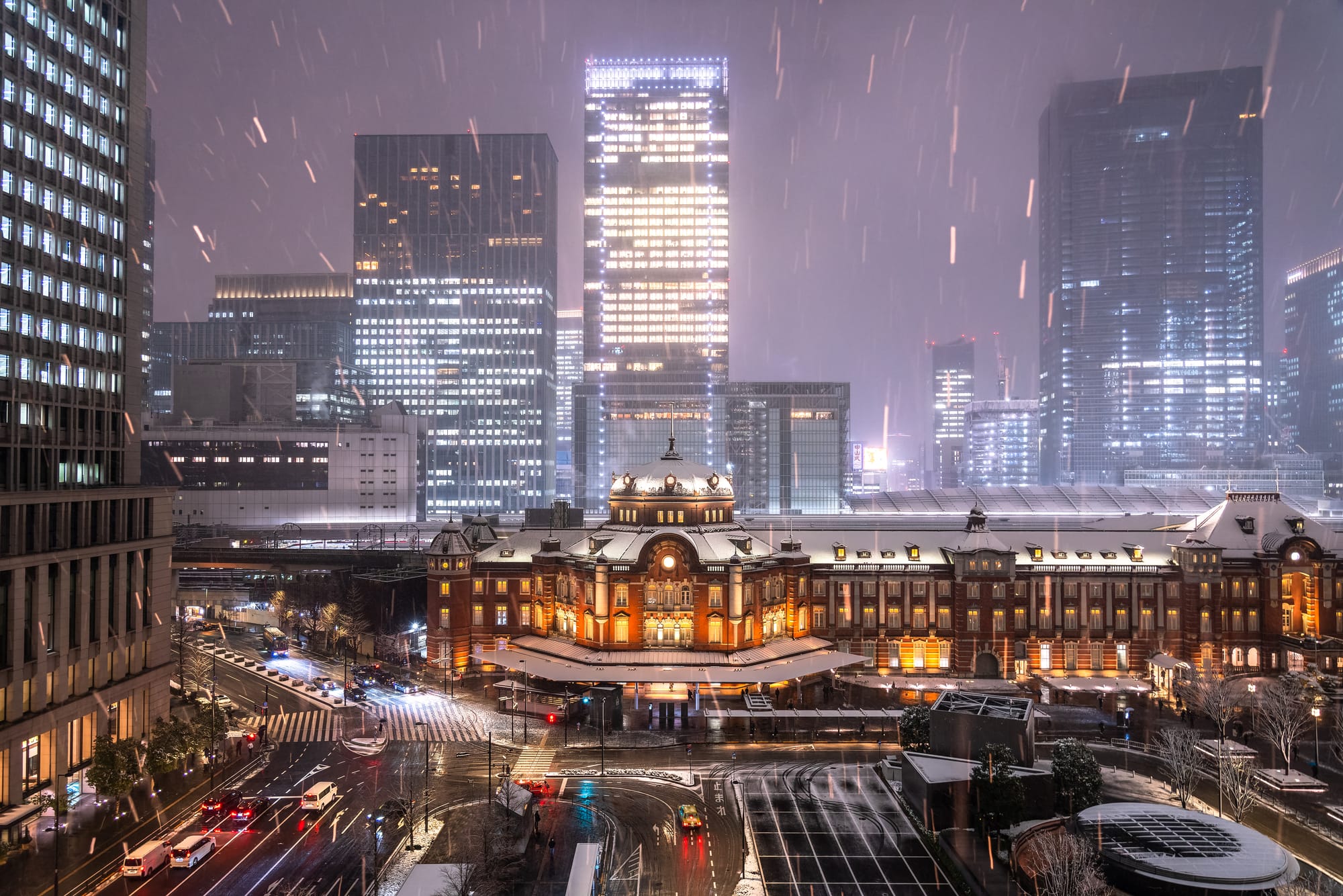 Snowy night cityscape featuring a Tokyo station, glowing warmly. 