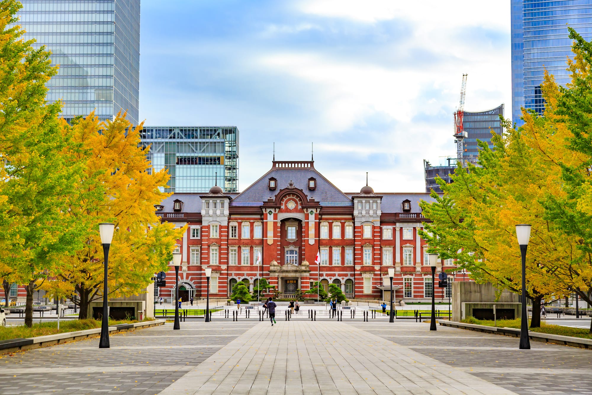 A view of Tokyo Station building from the front, with beautiful changing autumn leaves on either side.