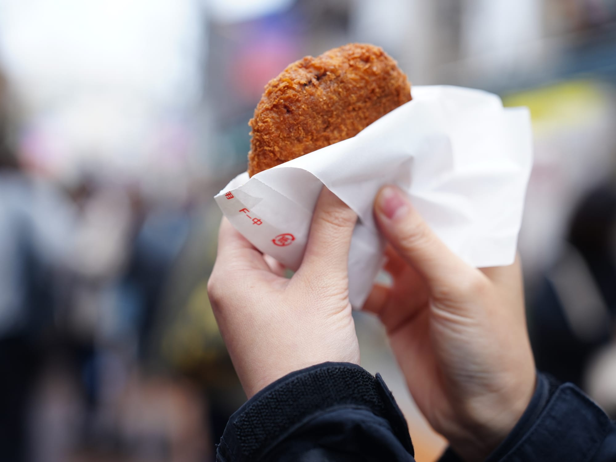 A person holding up menchi katsu (a fried Japanese snack)