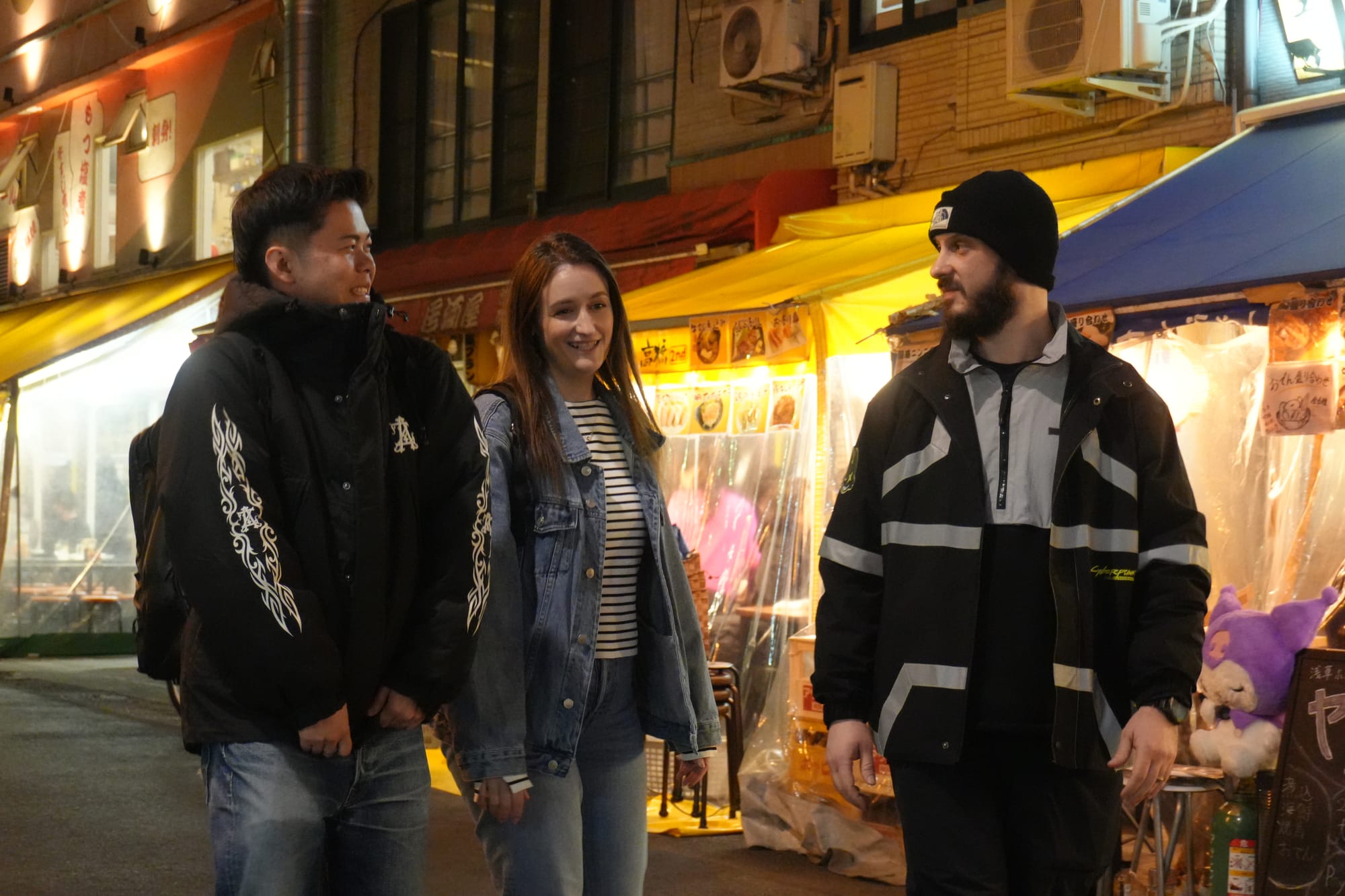 A smiling guide chatting with guests as they walk down a Tokyo street during one of TOMOGO!'s Japan bar-hopping tours