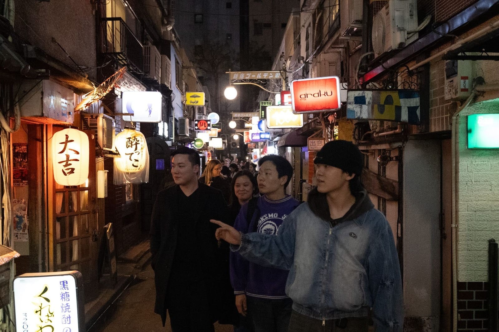 A guide pointing something out to amazed-looking guests as they walk down a Tokyo alley full of bars and pubs A smiling guide chatting with guests as they walk down a Tokyo street during one of TOMOGO!'s Japan bar-hopping tours