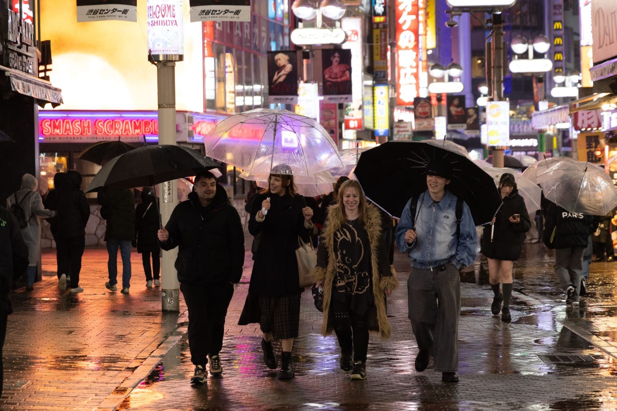 A guide and three guests while holding umbrellas while walking down Tokyo's Shibuya Center-Gai during one of TOMOGO!'s Japan bar-hopping tours