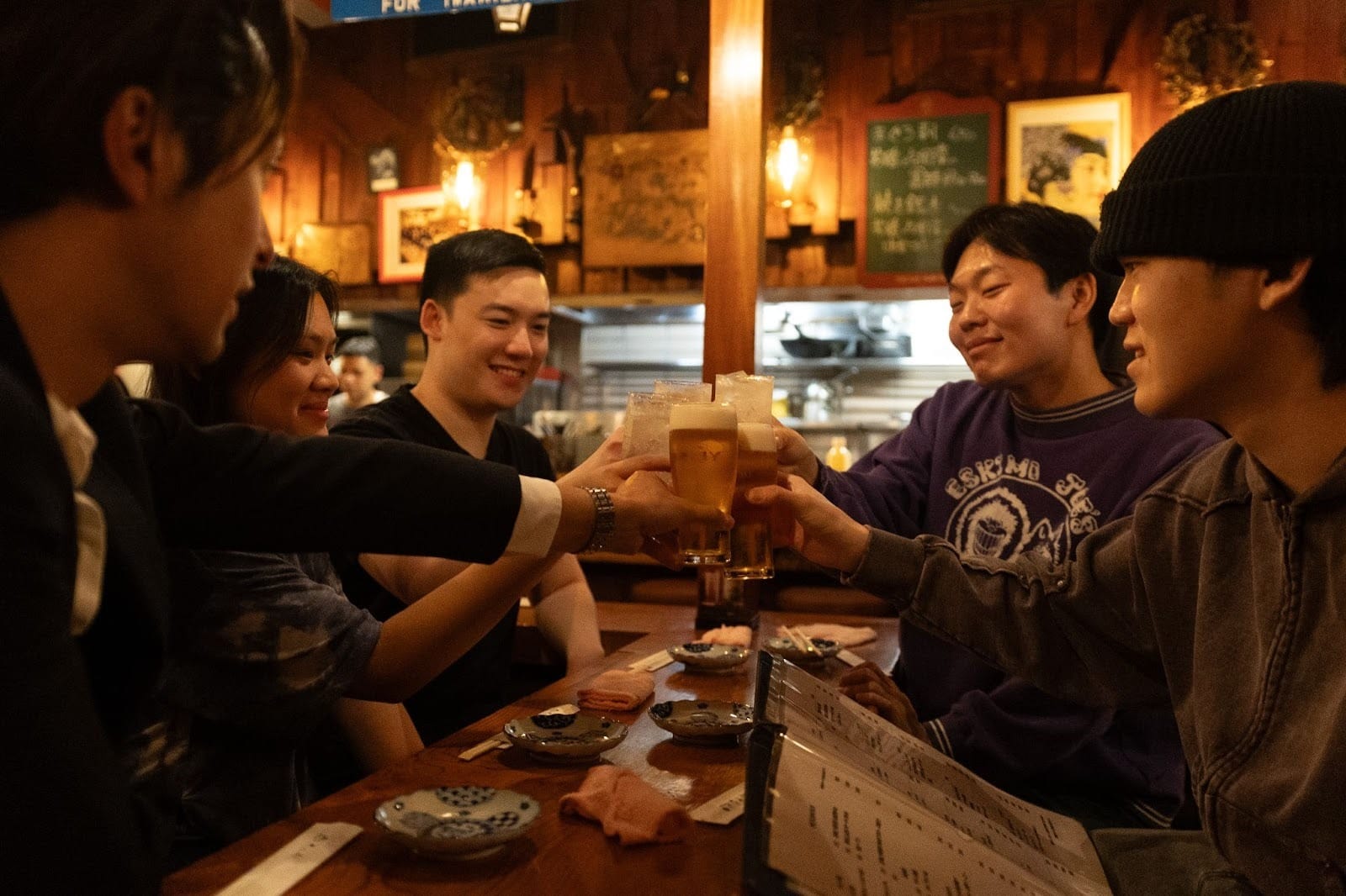 Guides and guests clinking their glasses and mugs for a toast at an izakaya during one of TOMOGO!'s Japan bar-hopping tours