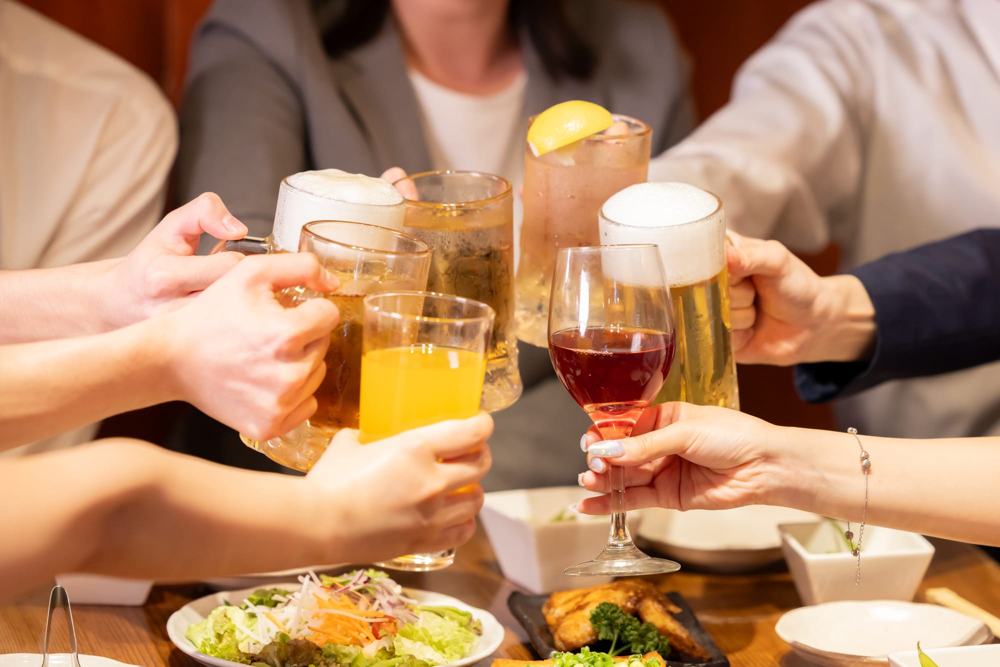 A group of diners, their faces obscured, clinking their glasses and mugs for a toast at an izakaya pub