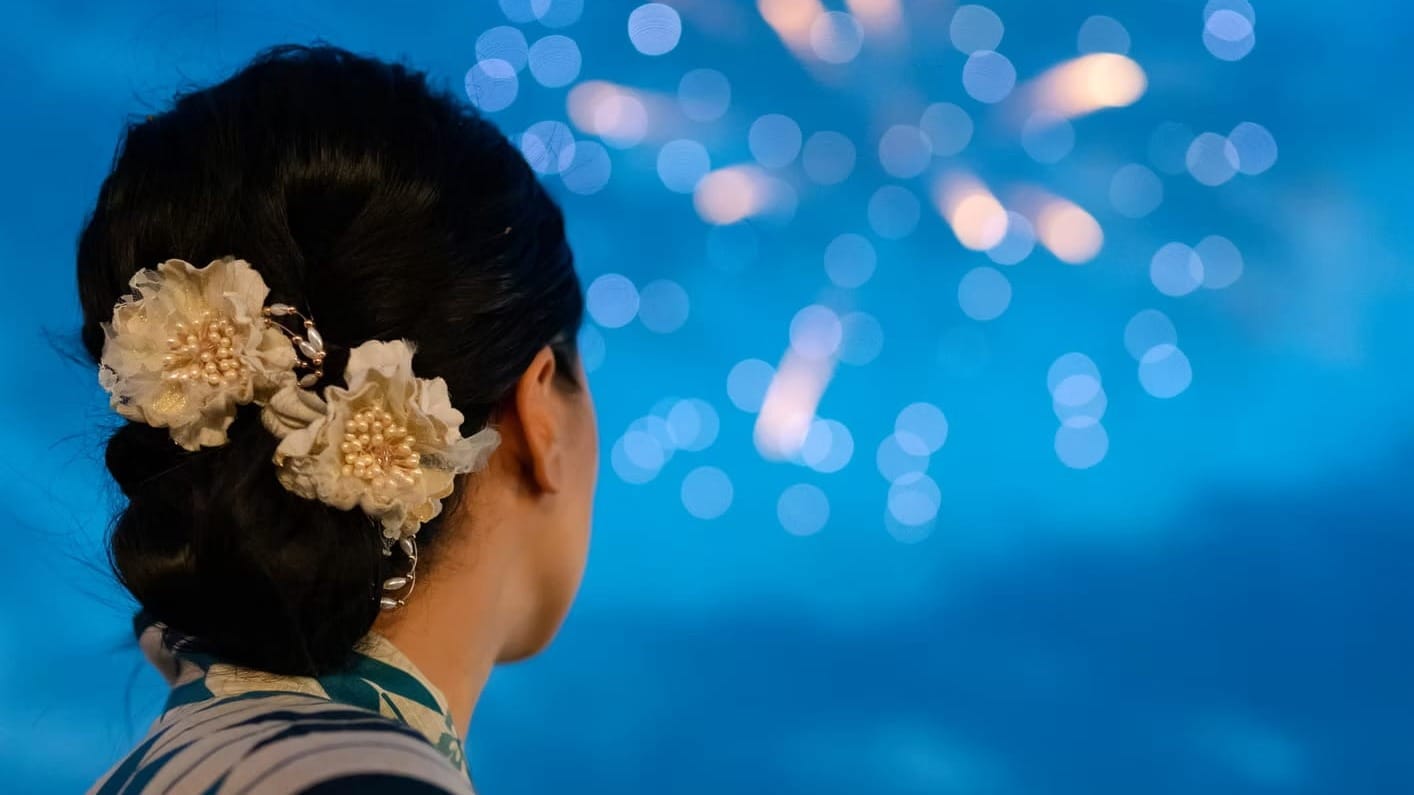 A girl looking at fireworks wearing a traditional Japanese kimono during a summer festival in Tokyo