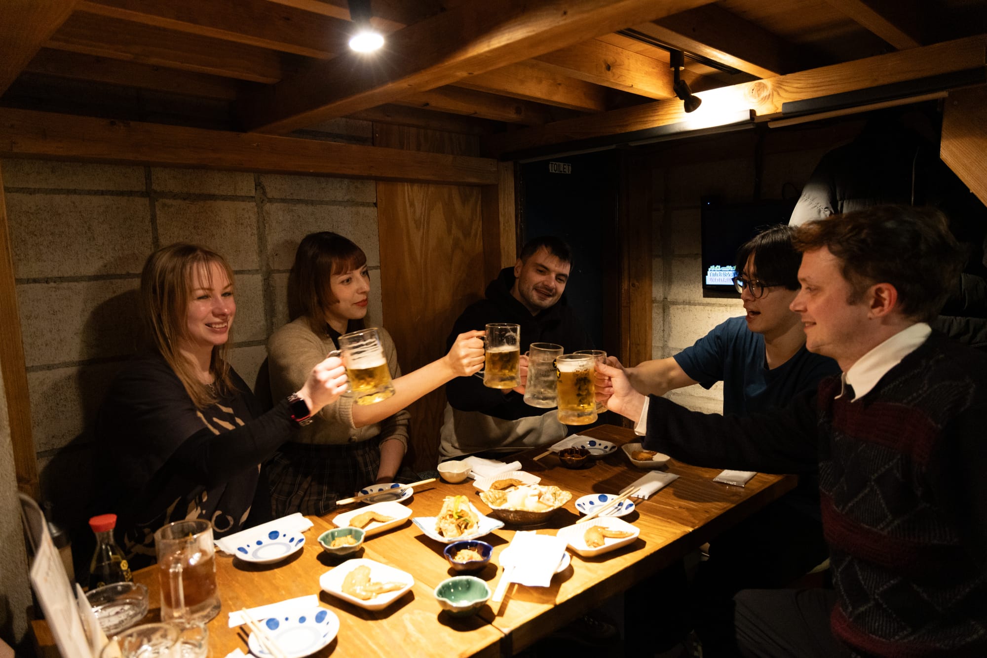 A group of friends in a Japanese izakaya toasting while eating