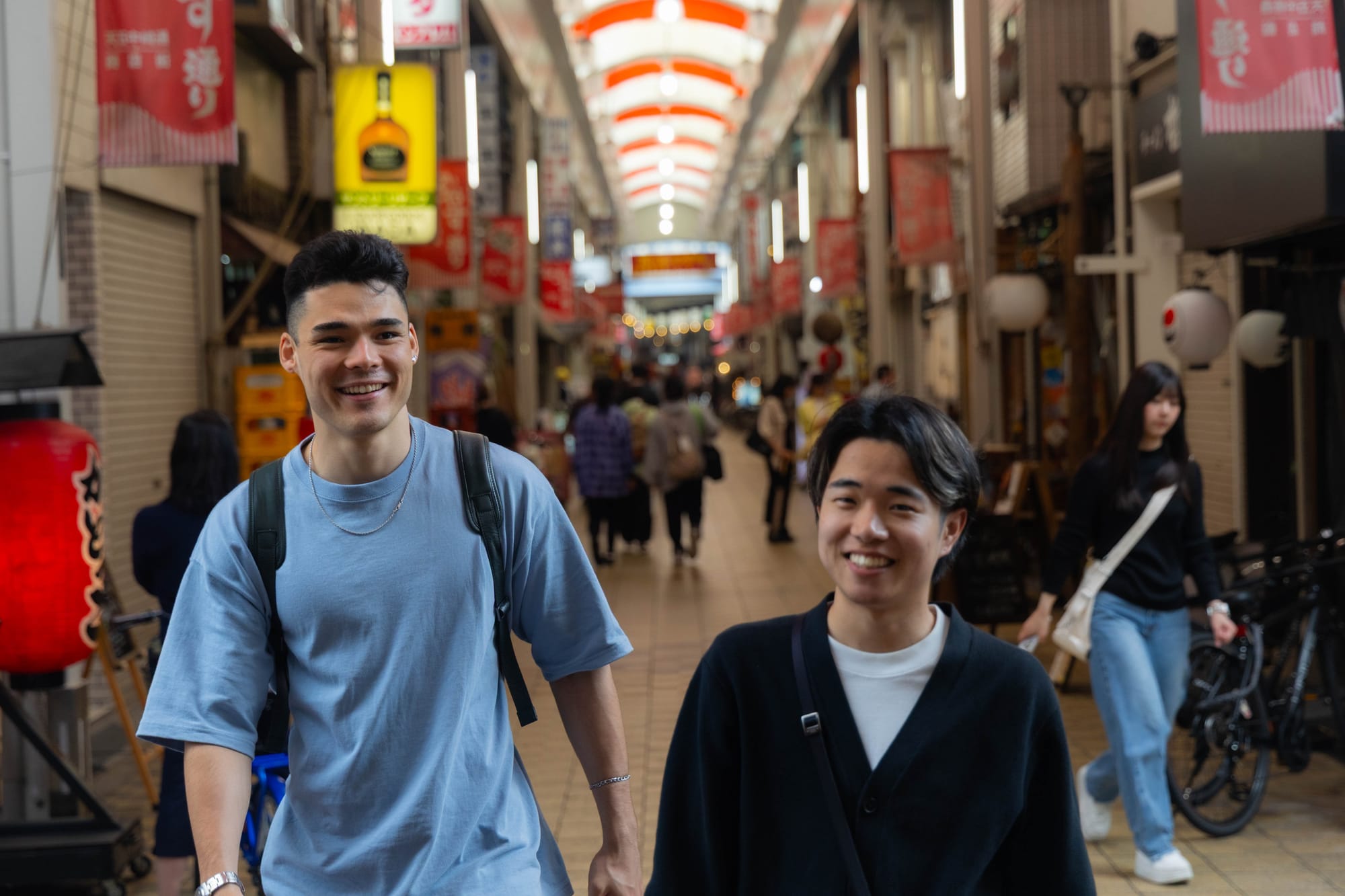 A tour guide shows their smiling guest around a market in Osaka