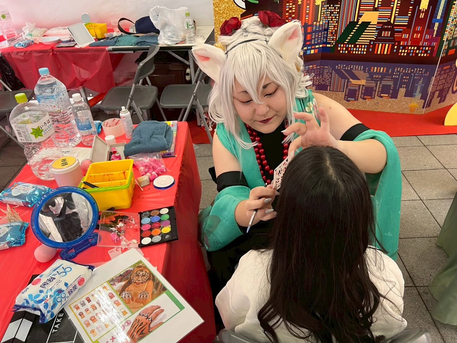 A face painter in cat ears paints a design on a visitor at the Bakeneko Festival.