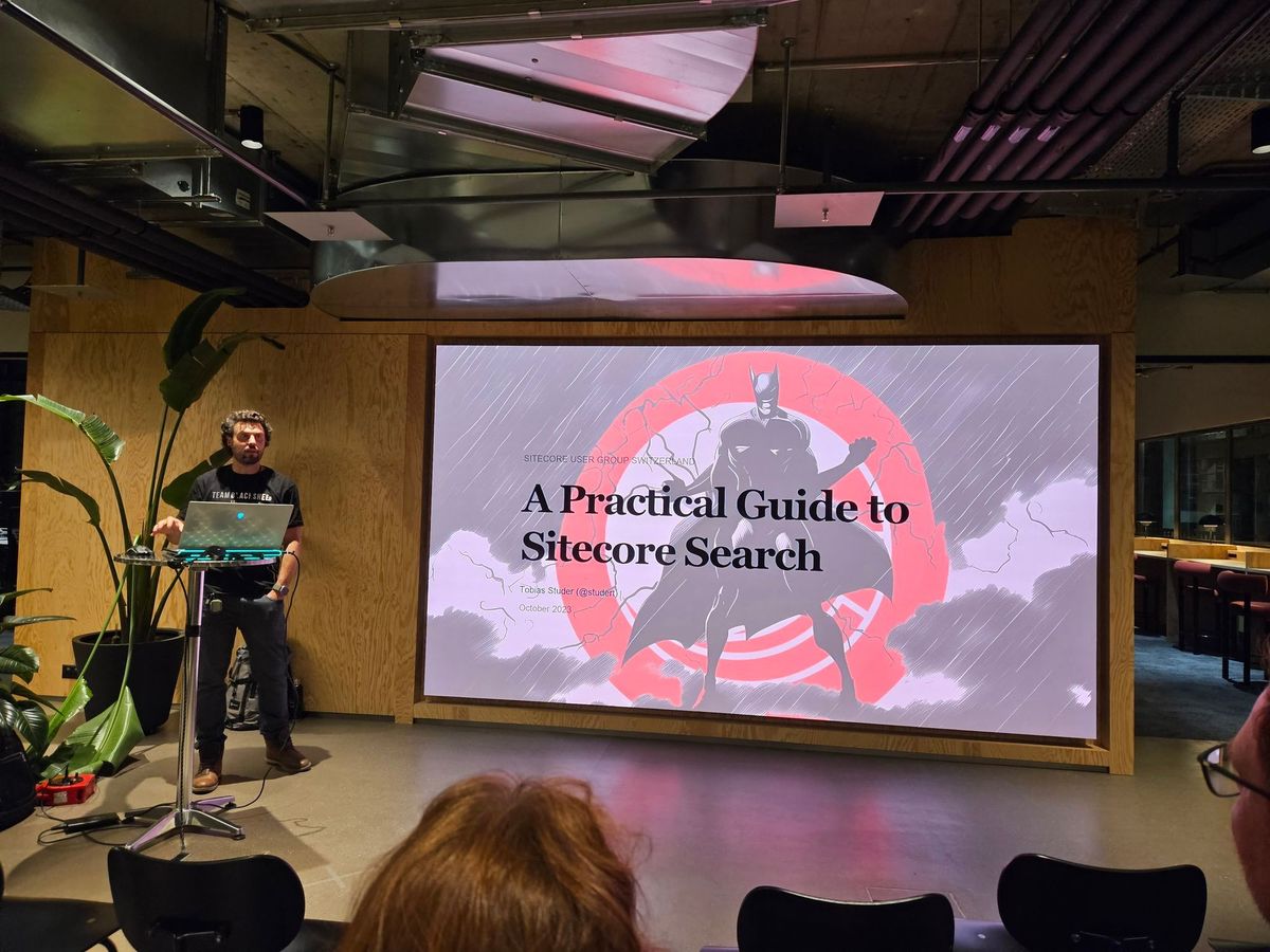 Tobias Studer behind a standing desk showing a slide from a presentation about Sitecore Search