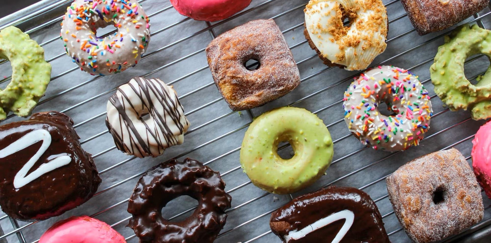 Colorful raspberry, pistachio, chocolate, cinnamon, etc. donuts on a wire tray