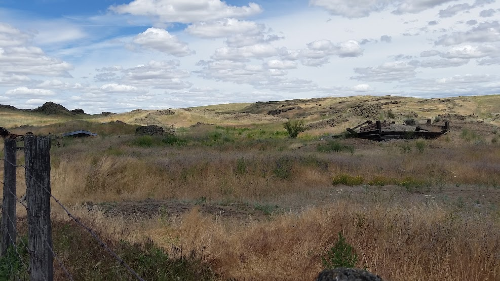 dry western rangeland with barbed wire fence and tumbling down enclosure 