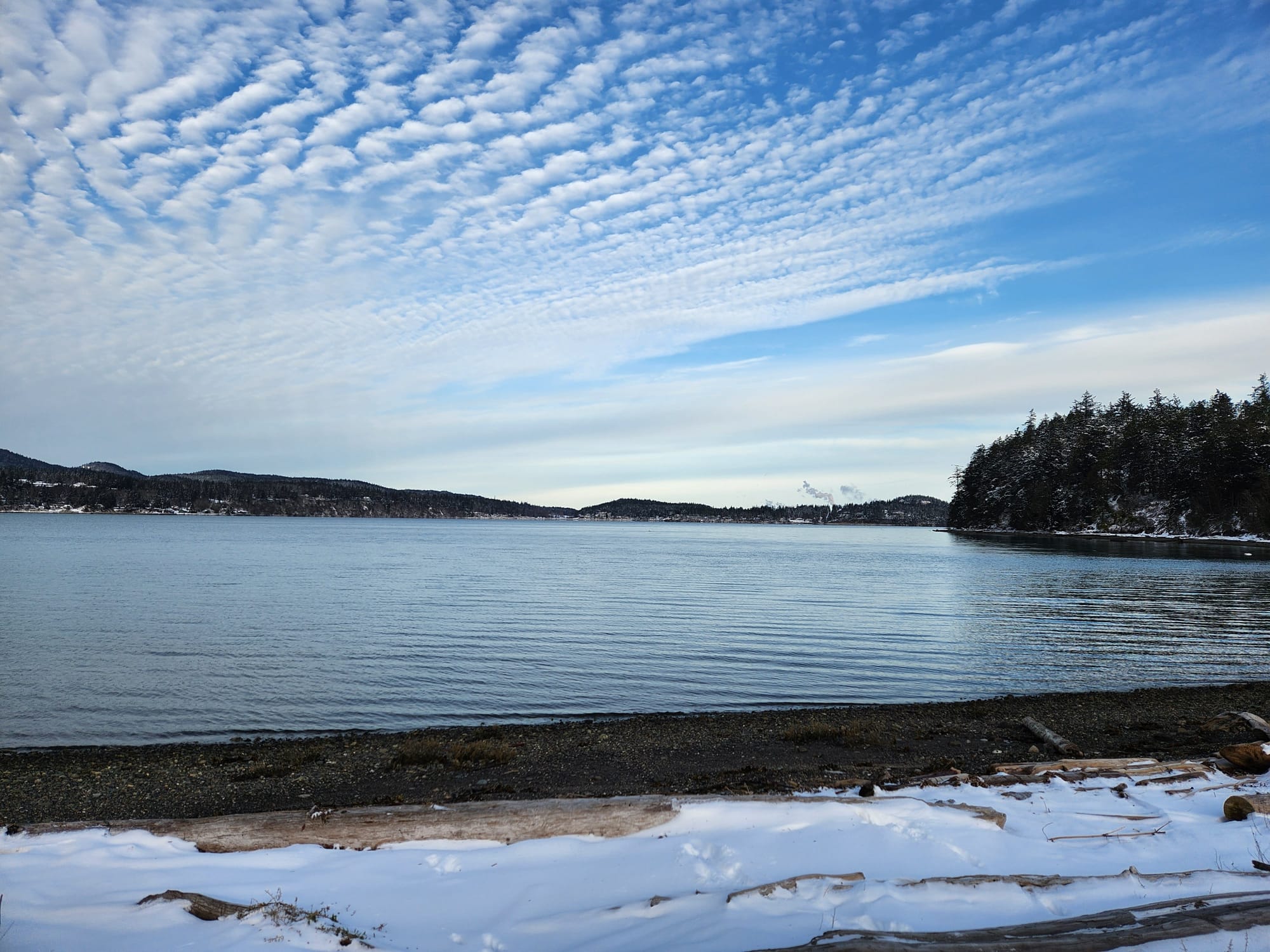 blue sky and scattered clouds above green island with effluent from unseen smokestacks