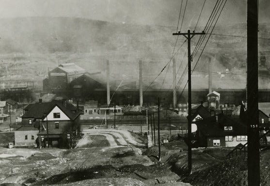 view down a hill toward a town, smokestacks, buildings, houses, lots of smoke