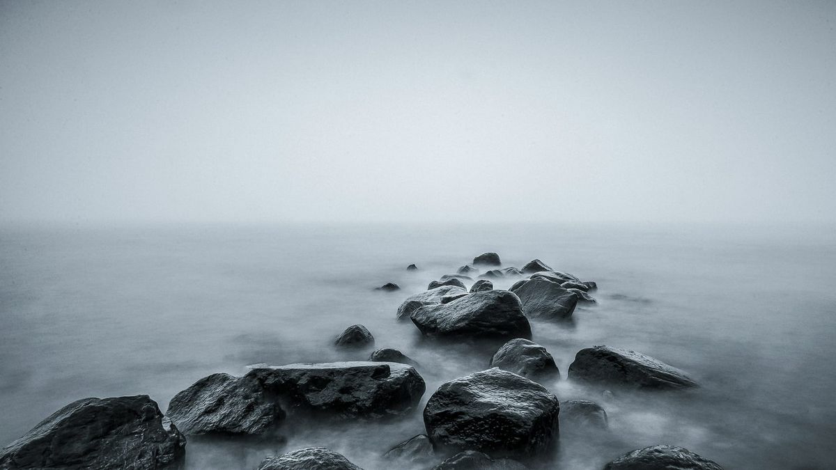 Large boulder outcropping extending into a gray and foggy body of water. The boulders are also gray in color.