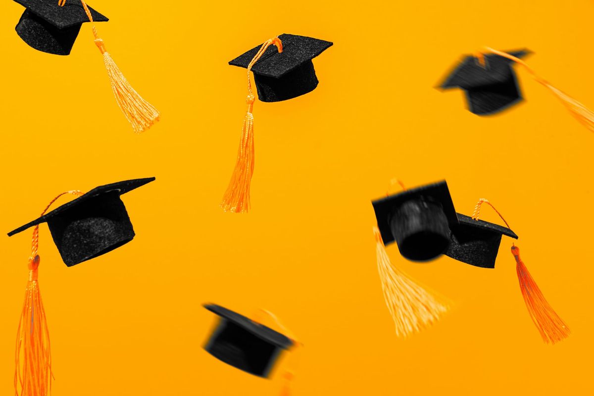 An image of black graduation caps with gold tassles in the air against an orange background.
